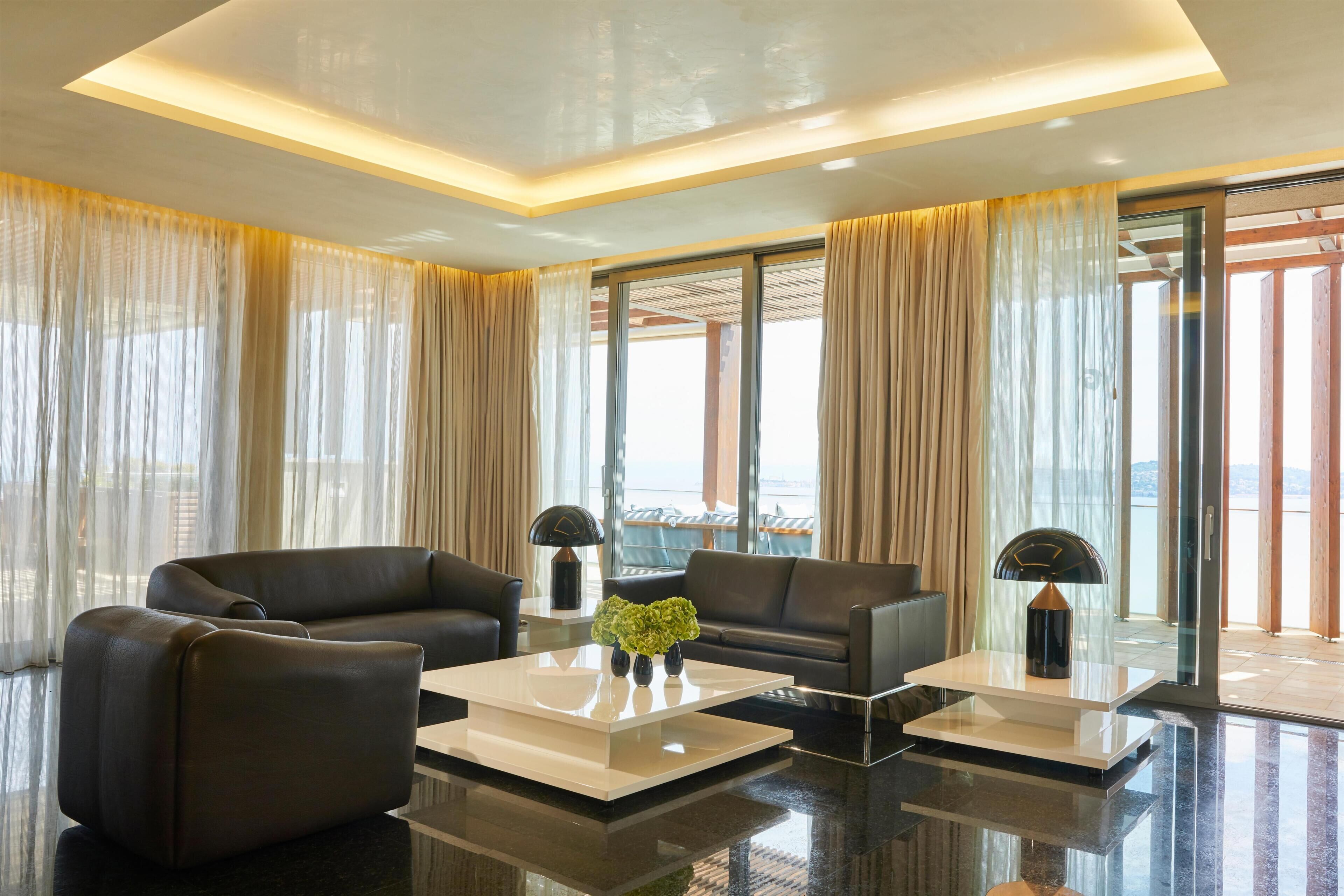 Ein modernes Wohnzimmer mit zwei schwarzen Sofas, einem weißen Couchtisch und einer Glastür, die auf einen Balkon führt.