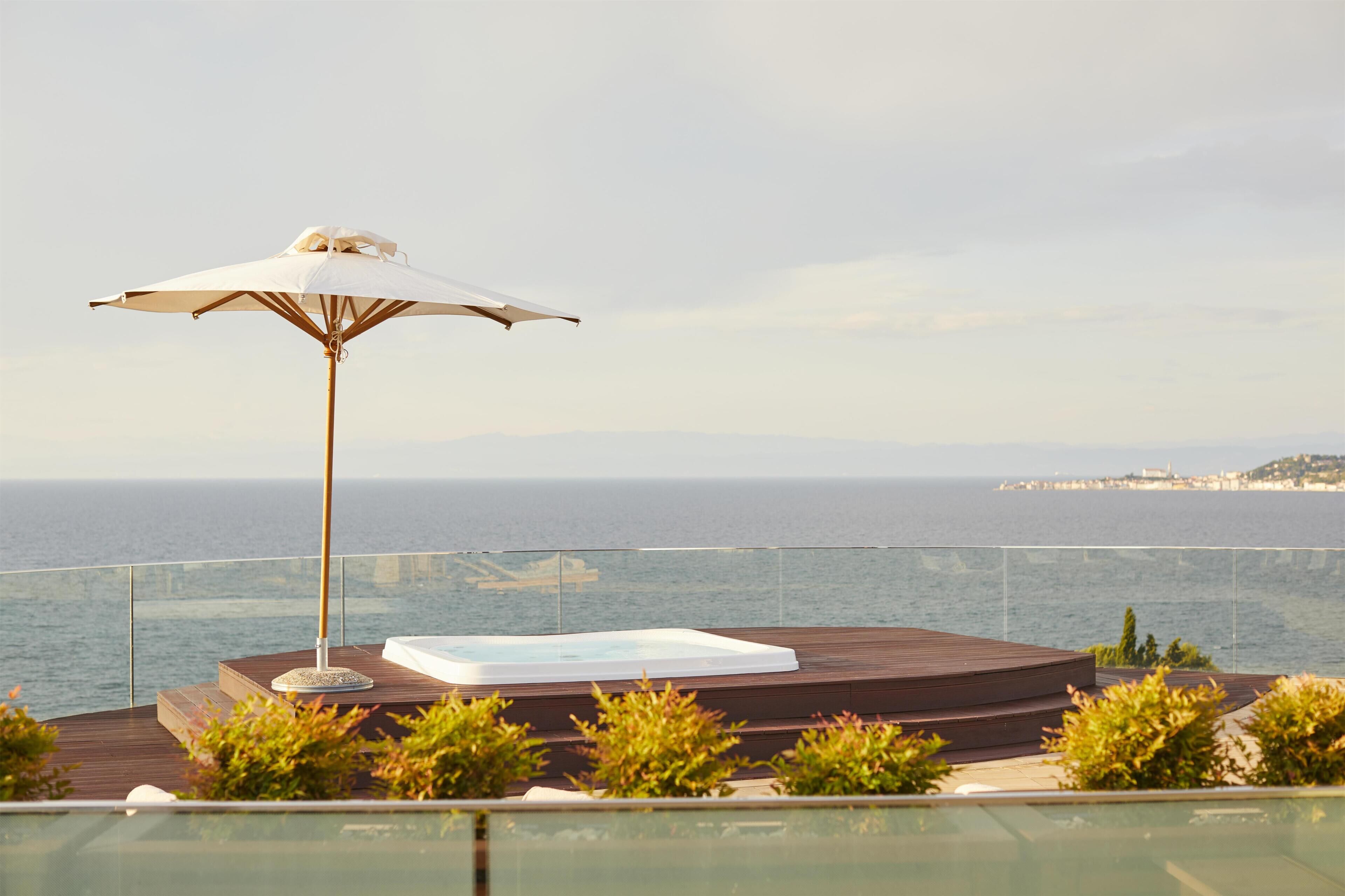 Eine Dachterrasse mit Whirlpool, Sonnenschirm und Meerblick.