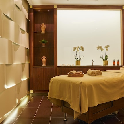 A spa room with a bed, shelves with plants, and a window with a view.