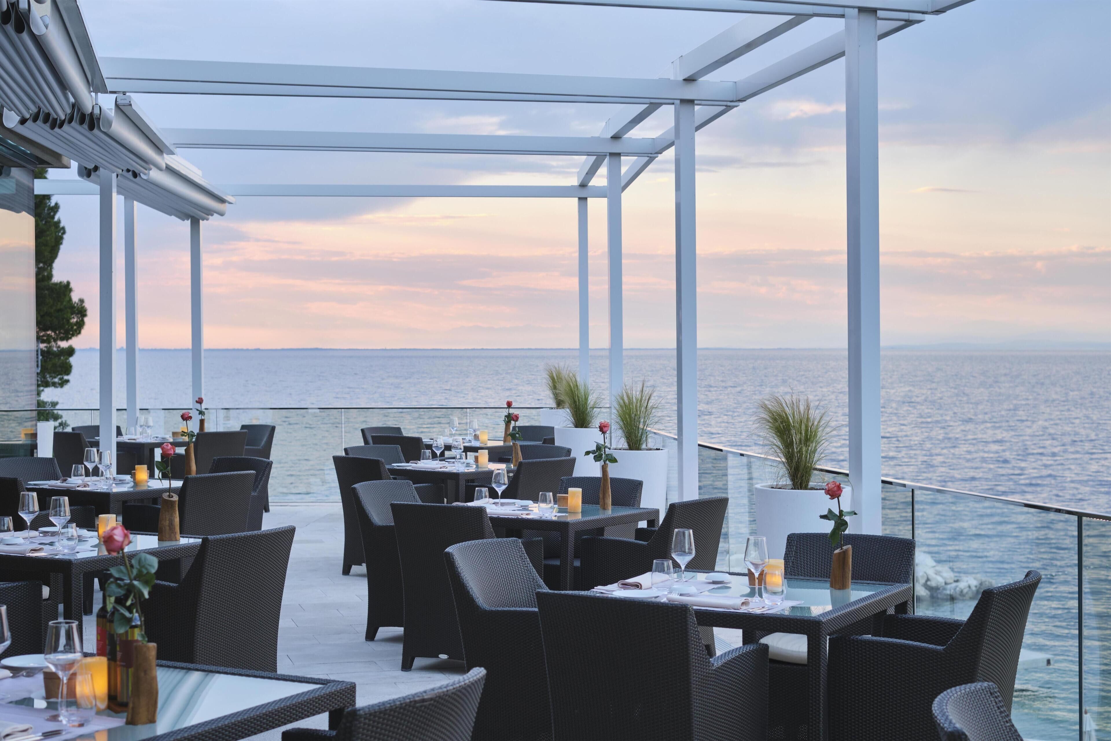 A seaside restaurant with outdoor seating, white columns, and a view of the sea.