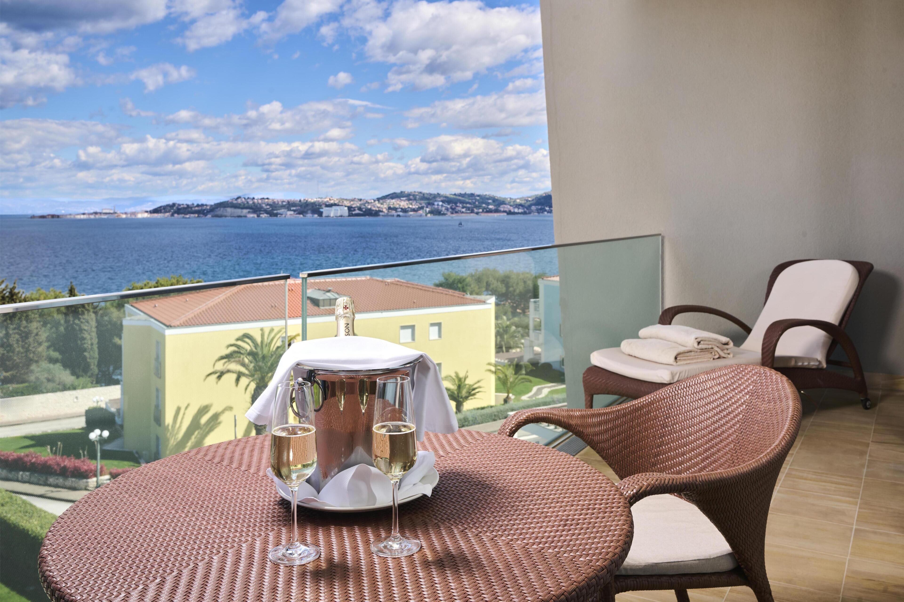 A balcony with wicker furniture, a table with a white cloth, and a view of the sea and buildings.
