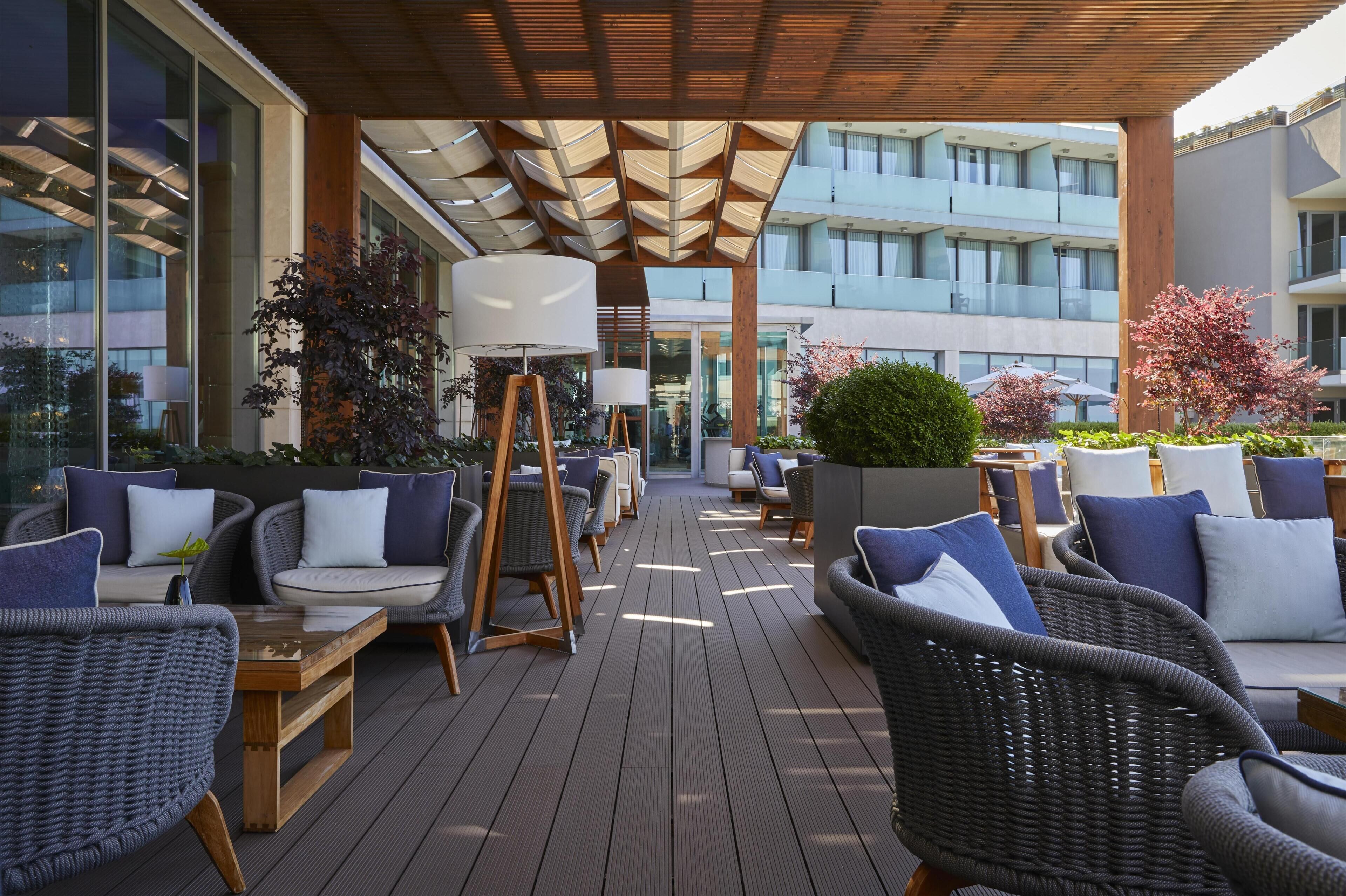 A covered outdoor seating area with wicker furniture, a wooden table, and potted plants.