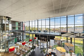 A spacious indoor area with multiple seating arrangements, large windows offering views of the outside, and a modern architectural design. - Aiden by Best Western Skavsta Airport (Nykoping)