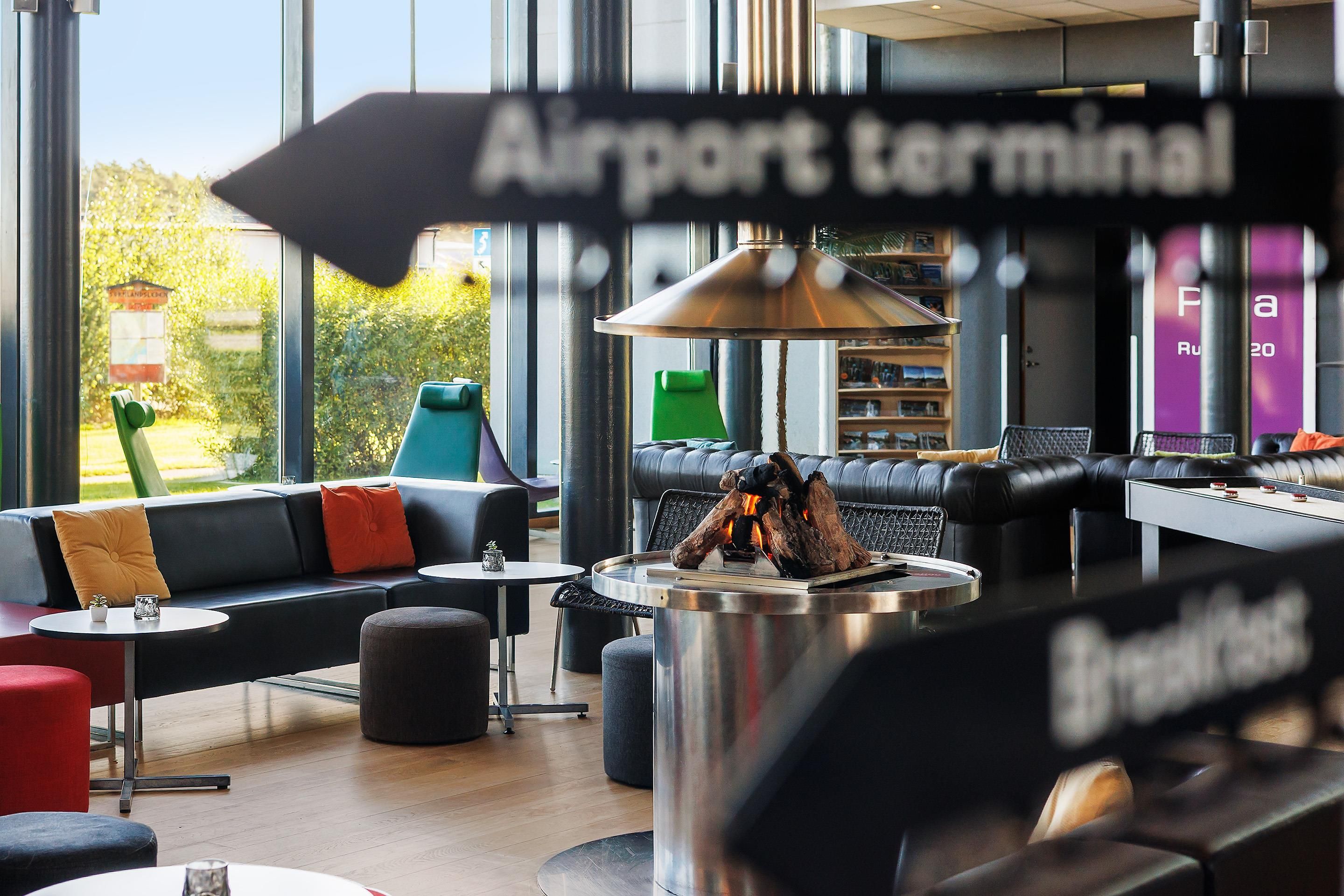 Un área de descanso con mesa de fútbol, asientos y vista al terminal del aeropuerto.