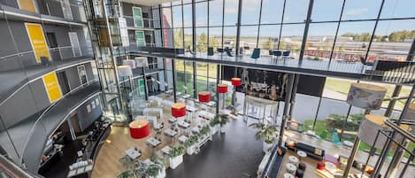 Un espacio interior de varios niveles con una zona central abierta, rodeada de asientos y mesas, y grandes ventanales que ofrecen vistas al exterior.