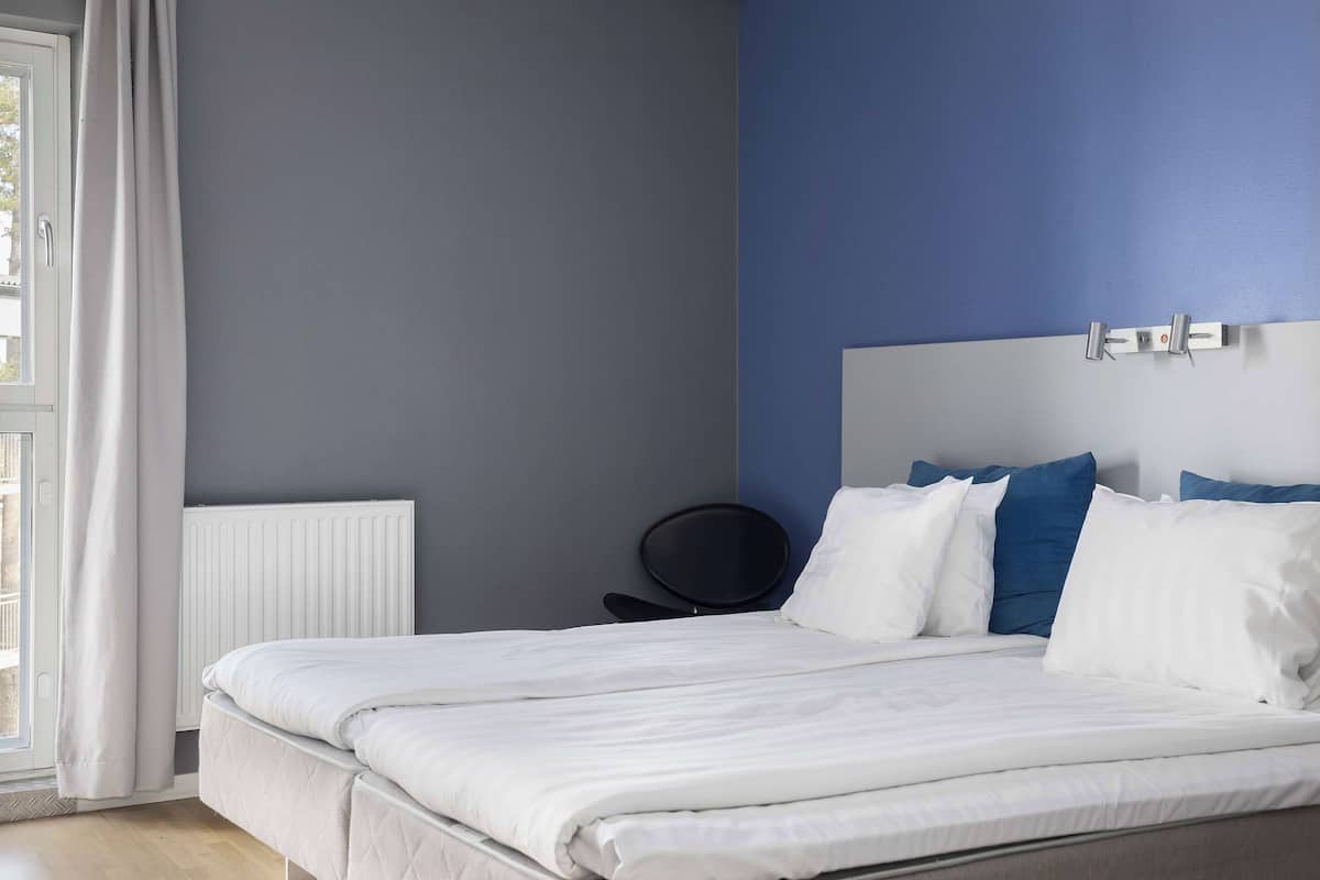 A neatly made bed with white bedding, a black chair, and a blue wall.
