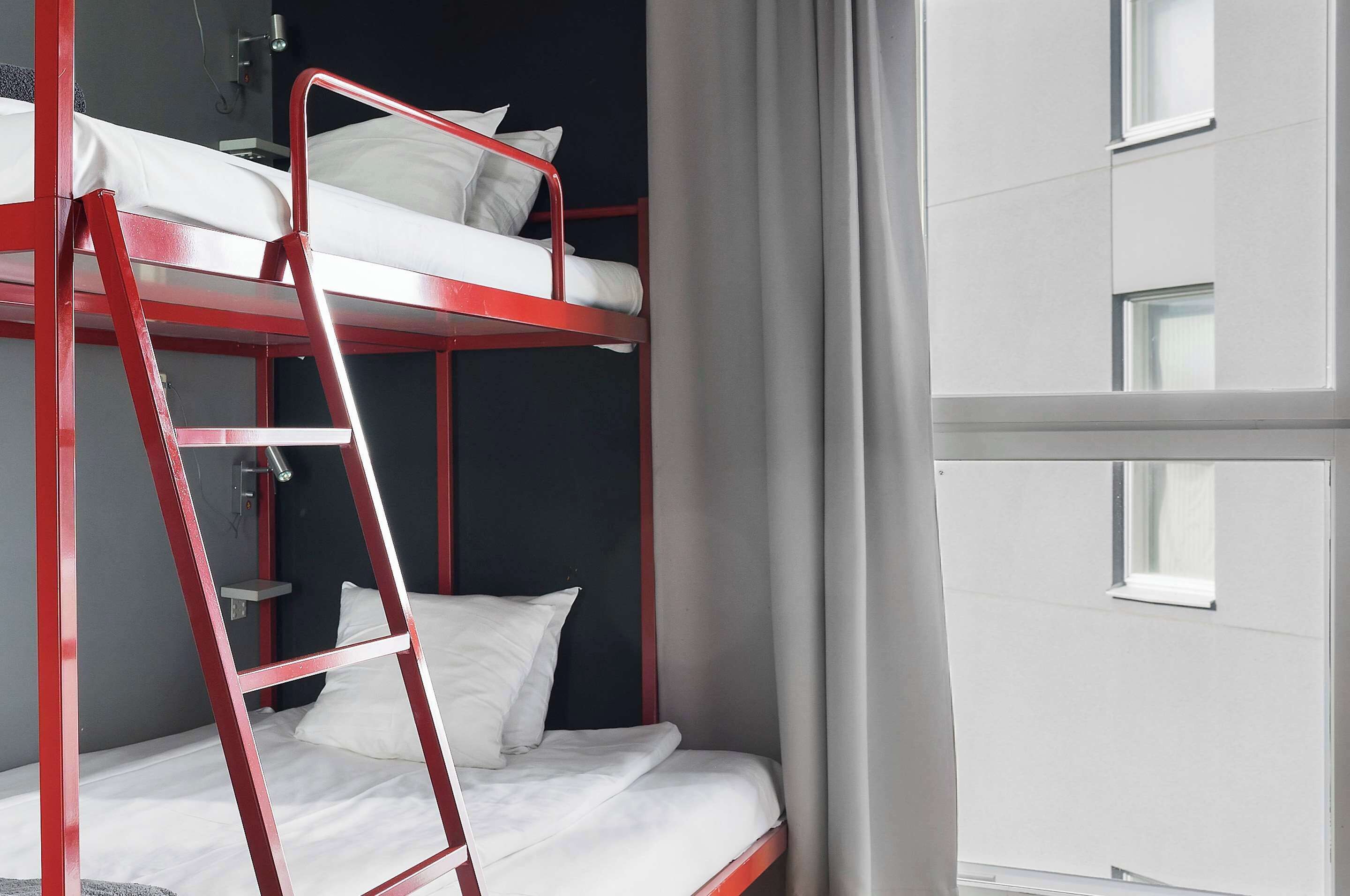 A bunk bed with a ladder, white bedding, and a window with curtains.