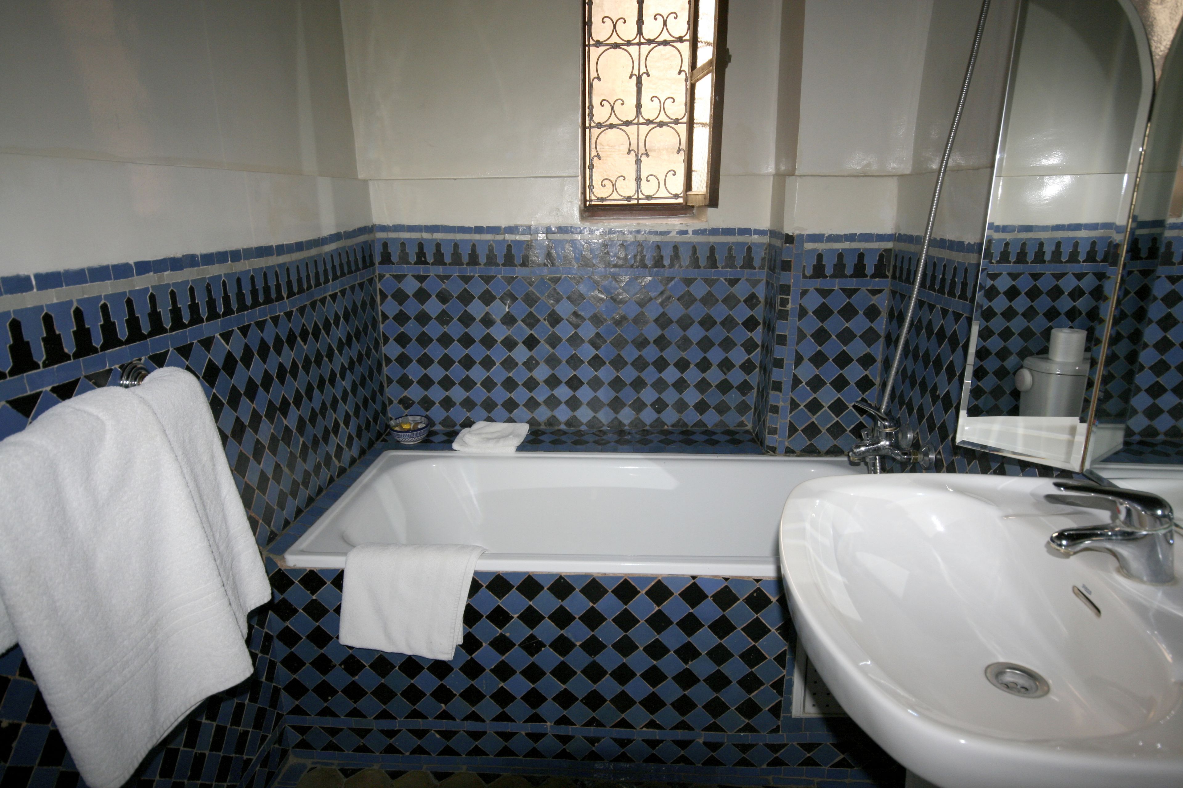 Un baño con bañera, lavamanos y una ventana con celosías decorativas.