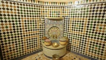 Un baño con piso de baldosas a cuadros, un diseño decorativo en la pared y un lavamanos con varios recipientes.