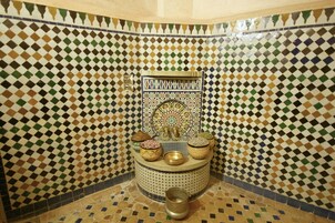 Un baño con piso de baldosas a cuadros, un diseño decorativo en la pared y un lavamanos con varios recipientes.