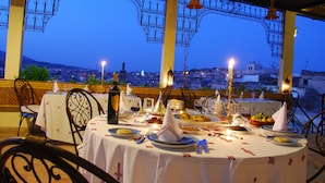 An outdoor dining area with tables set for a meal, overlooking a cityscape at dusk.