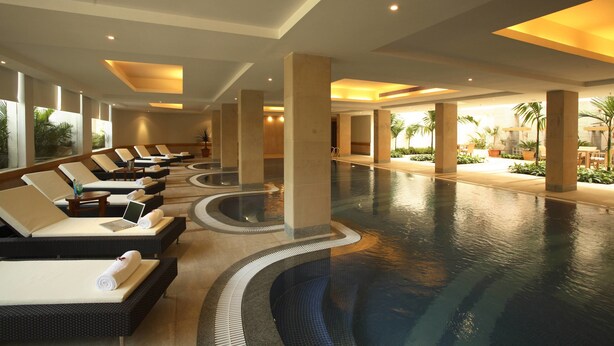 A large indoor swimming pool with lounge chairs and sunbeds, surrounded by pillars and potted plants. - Ellaa Hotel Gachibowli (Hyderabad)