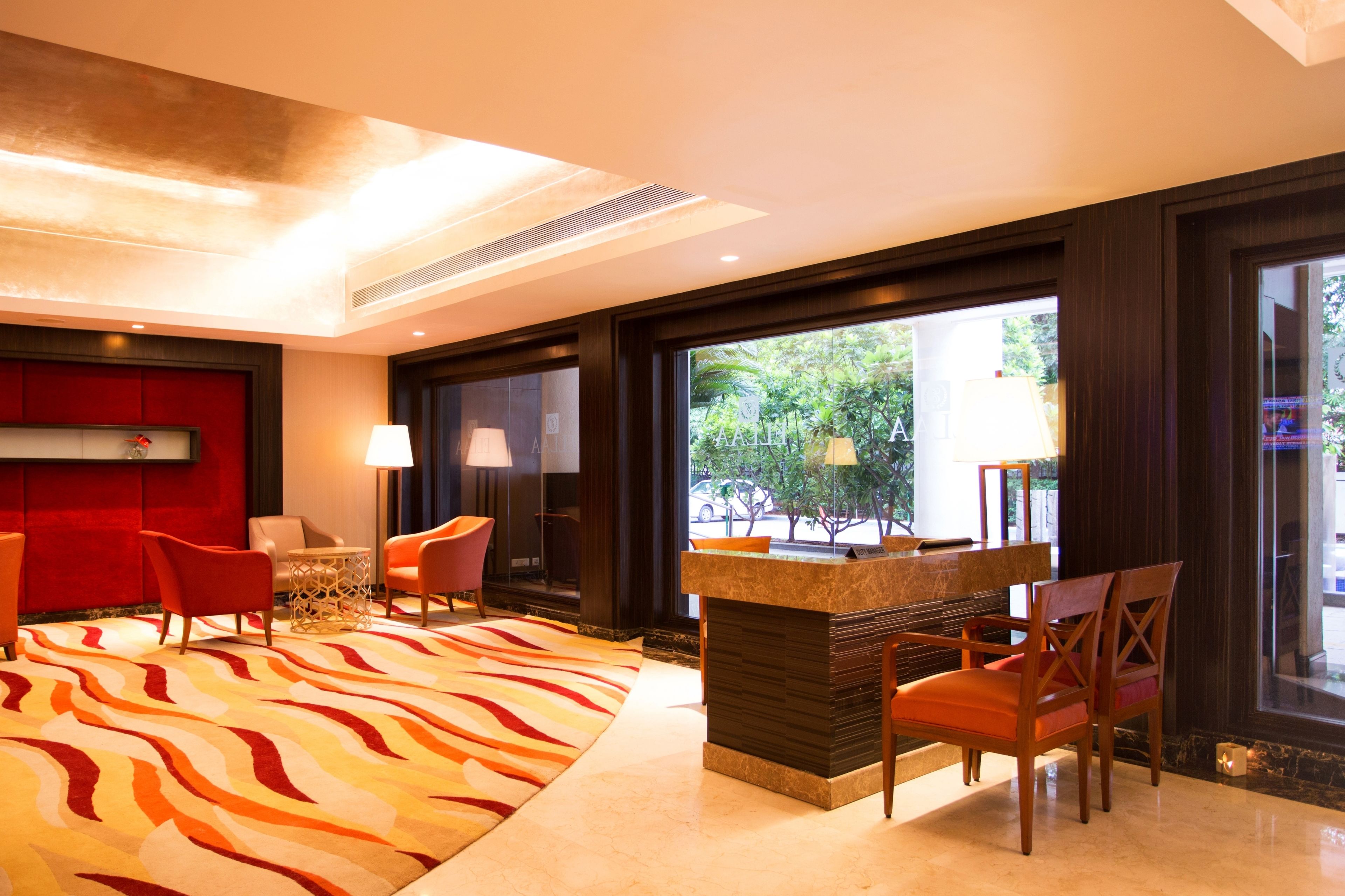 A lobby with a reception desk, seating area, and large windows offering a view of greenery.