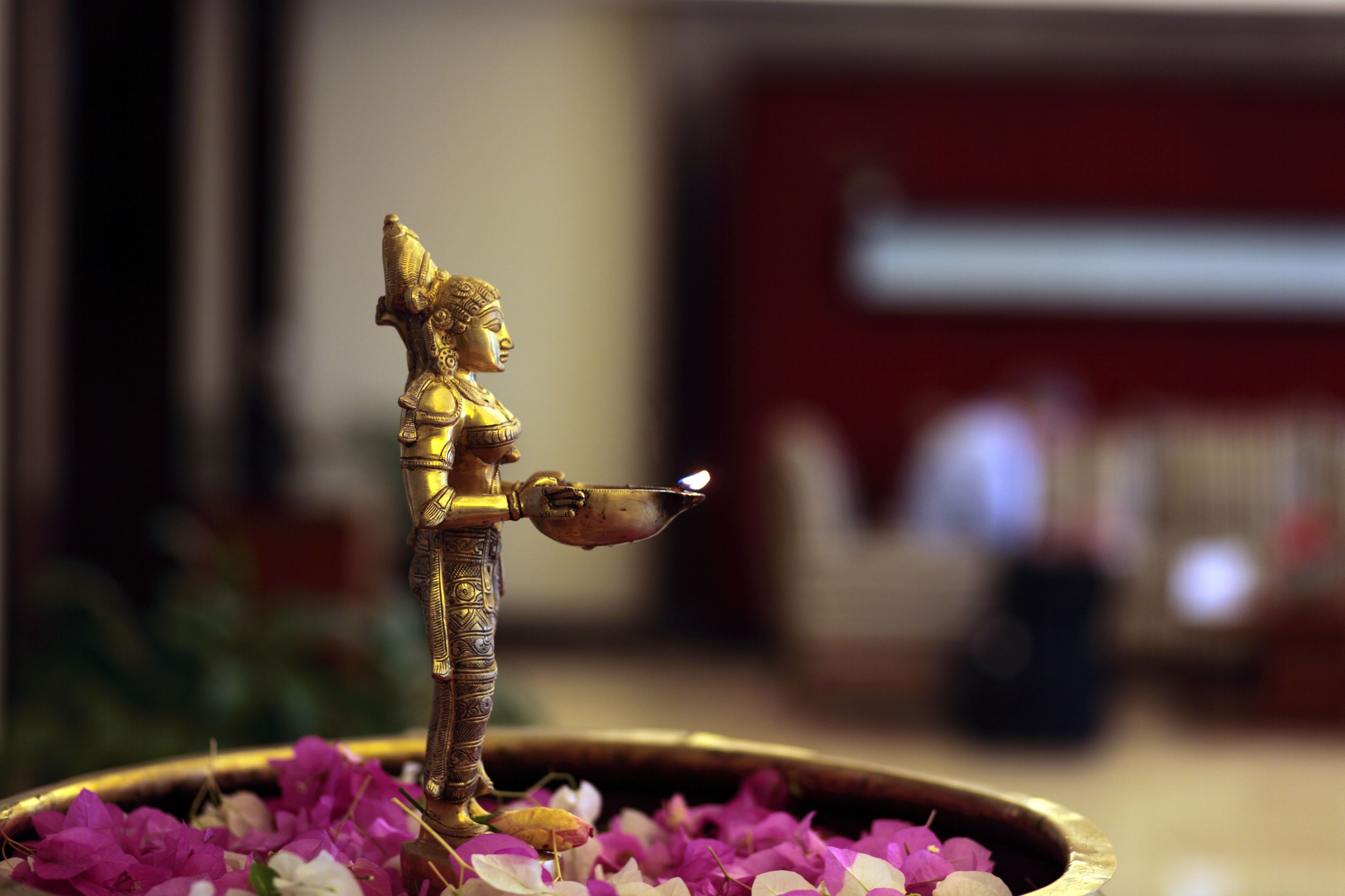 Eine Bronzestatue einer Gottheit, die eine Laterne hält, umgeben von Blumen.