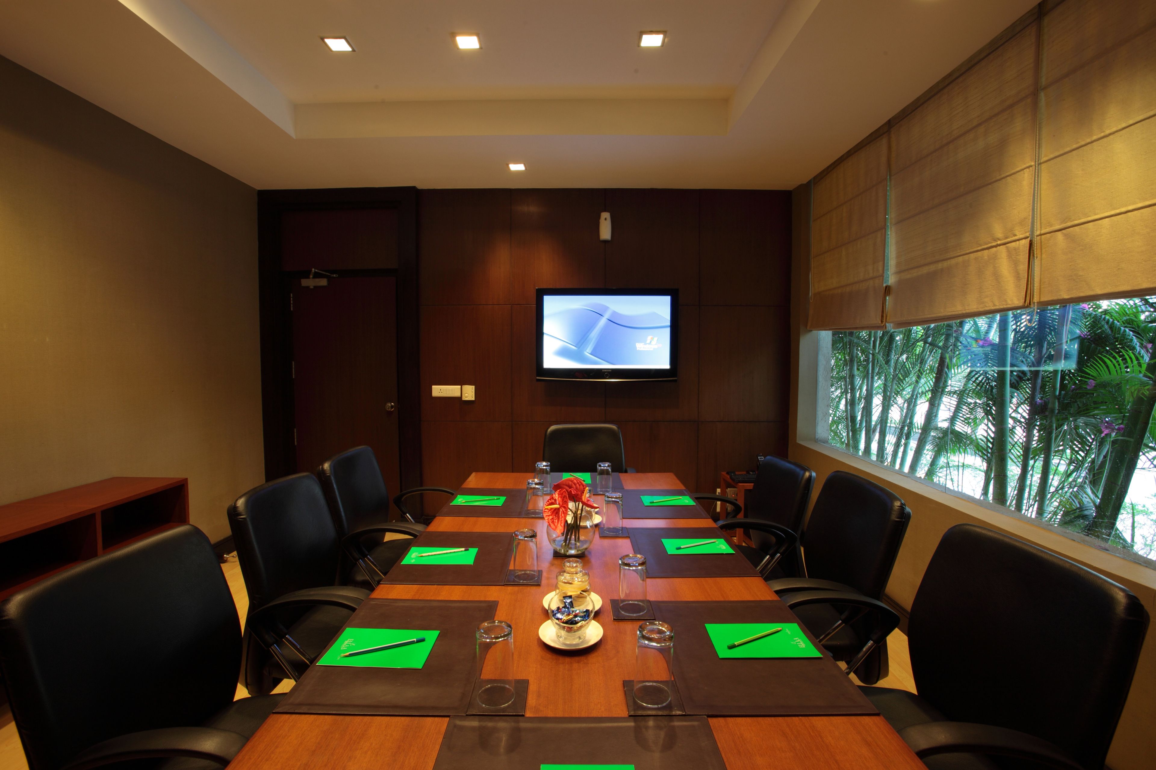 A conference room with a long table, chairs, a television, and a window with a view of palm trees.