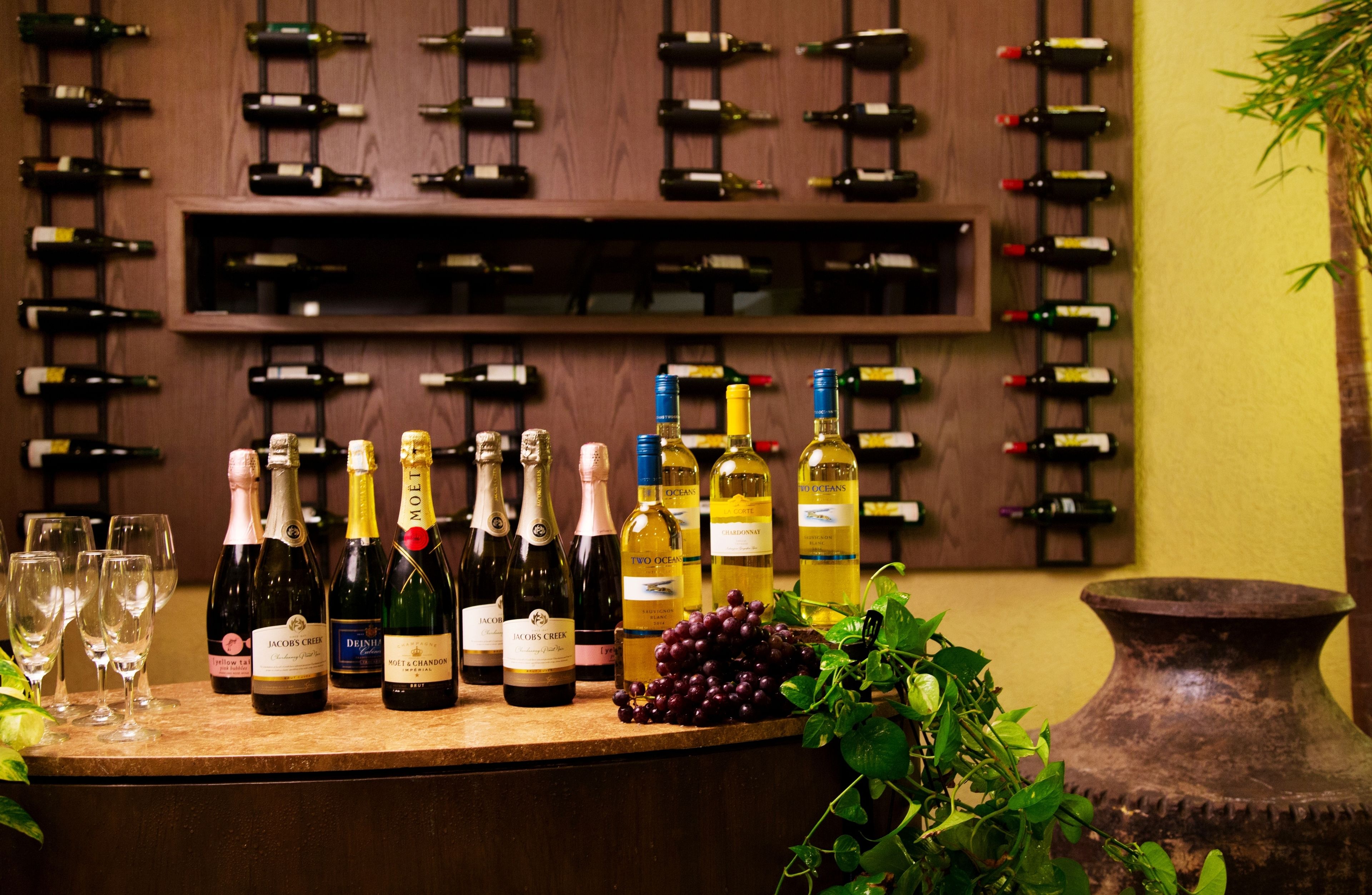 Zona de degustación de vinos con botellas y copas sobre una barra, rodeada por un muro de madera con más botellas.