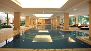 An indoor swimming pool with clear water, sunlit ceiling, and lounge chairs along the sides. - Ellaa Hotel Gachibowli (Hyderabad)