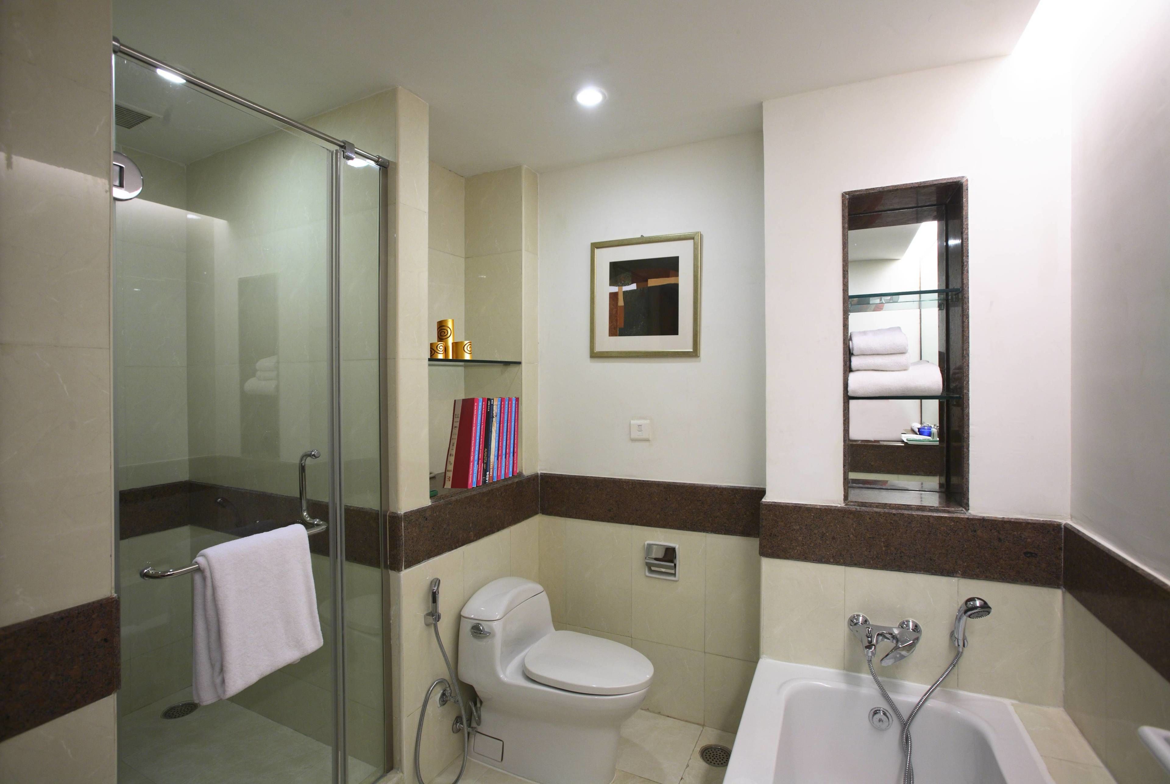 A bathroom with a glass shower enclosure, a toilet, a bathtub, and a small shelf with toiletries.