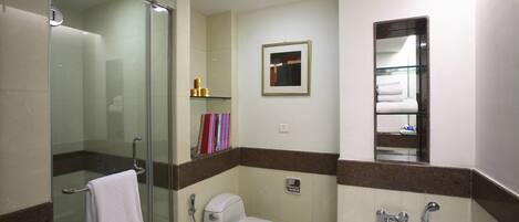 A bathroom with a glass shower enclosure, a toilet, a bathtub, and a small shelf with toiletries.