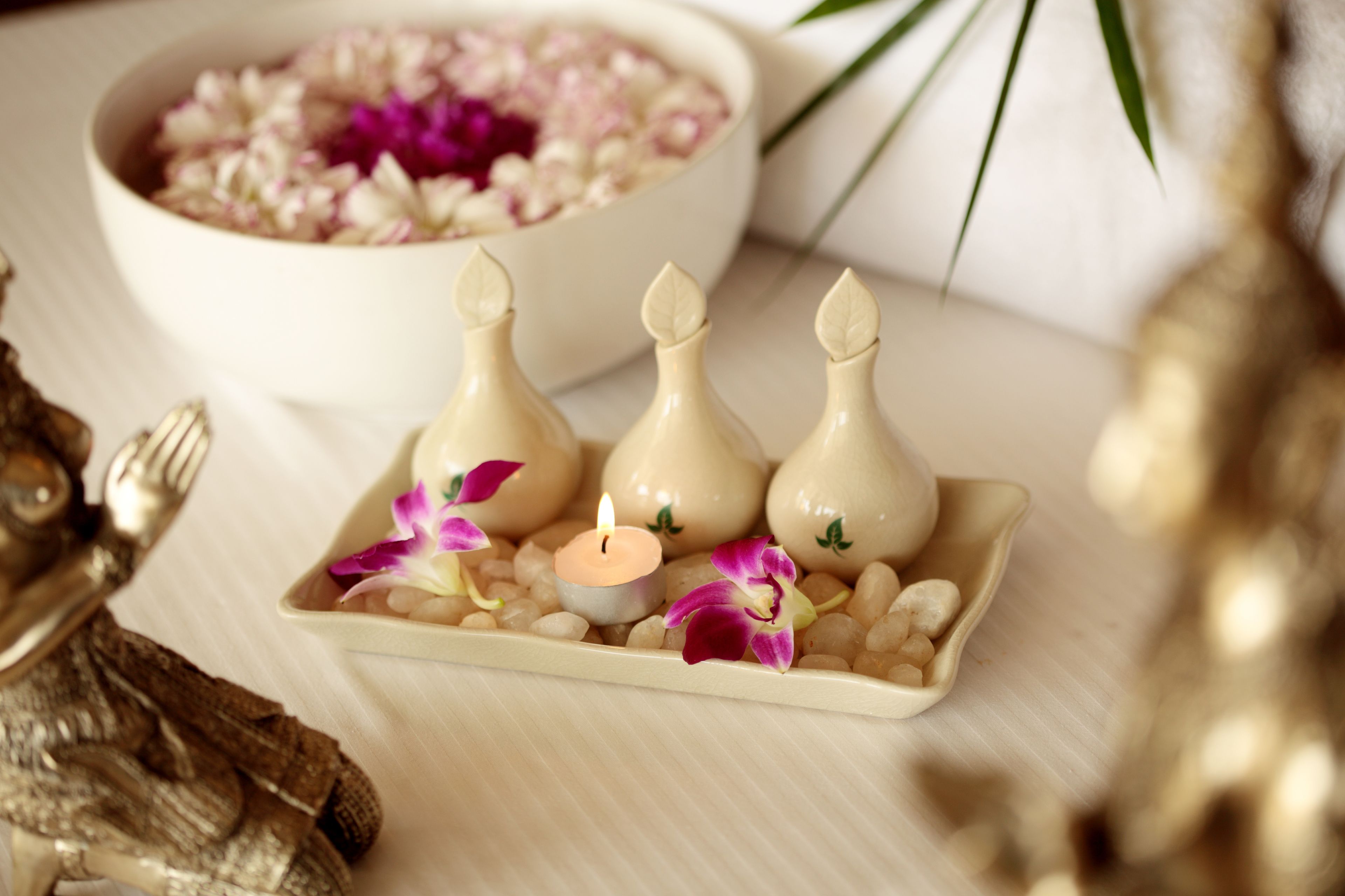 Un plateau contenant trois récipients en forme de bougie, une bougie allumée et des fleurs décoratives, le tout posé sur une surface texturée.