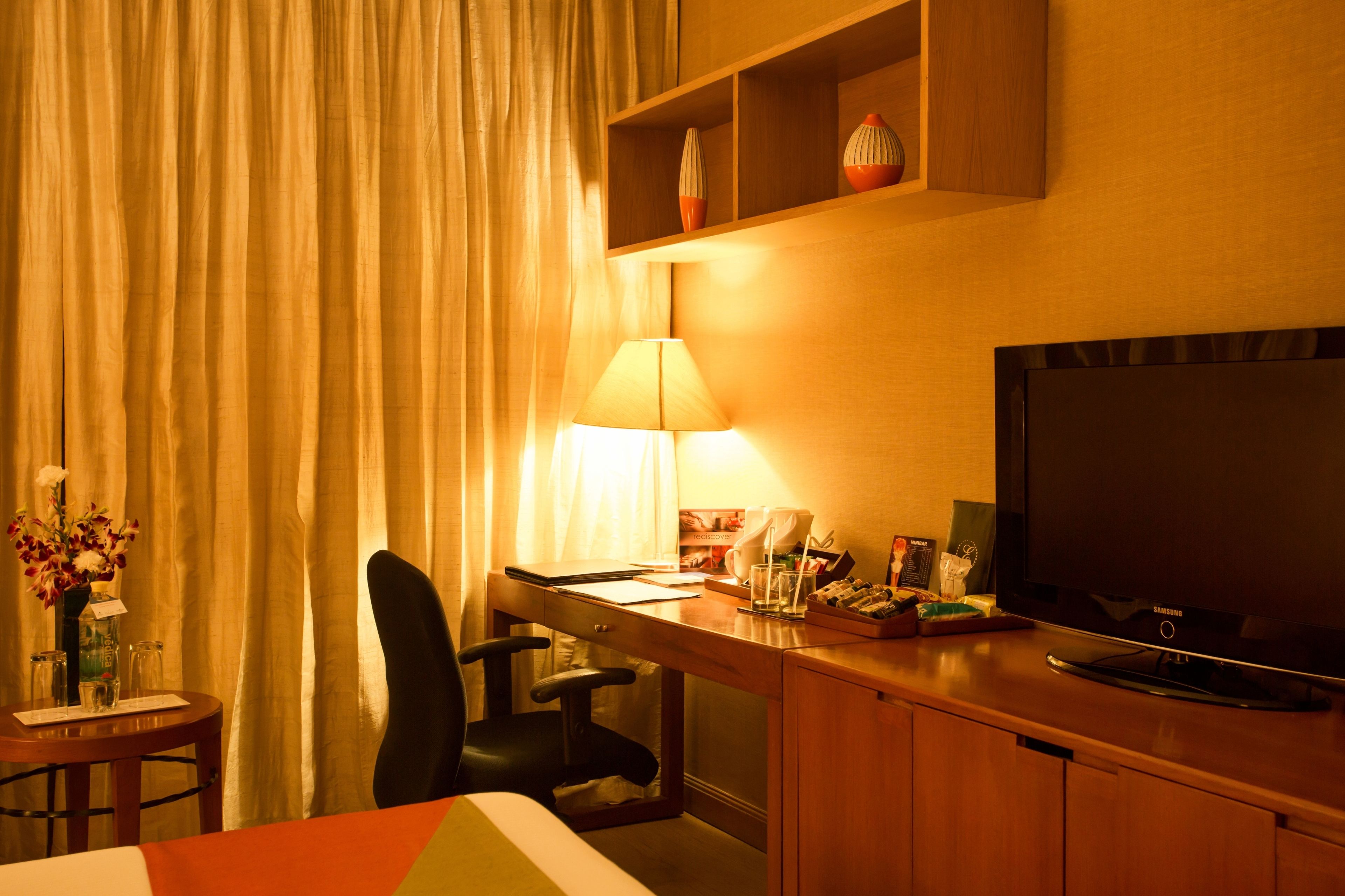 Habitación de hotel con cama, escritorio con lámpara, televisión y una pequeña mesa con un florero.