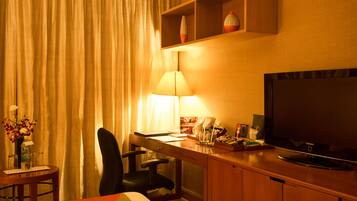 Habitación de hotel con cama, escritorio con lámpara, televisión y una pequeña mesa con un florero.