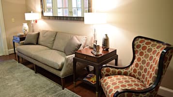 Una sala de estar con un sofá, un sillón estampado, una mesita con una lámpara y un espejo en la pared.