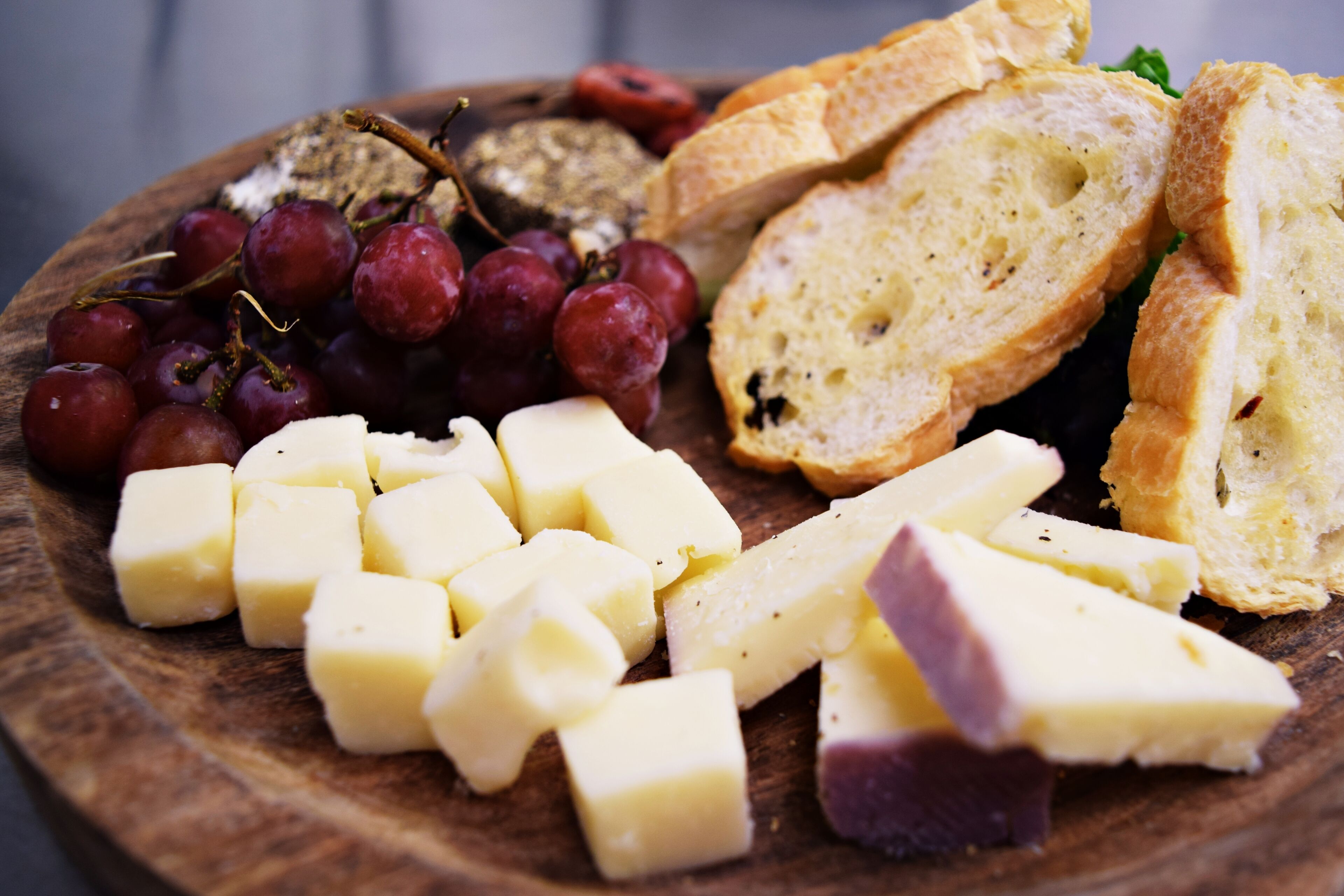 A wooden board with cheese, grapes, and bread slices.
