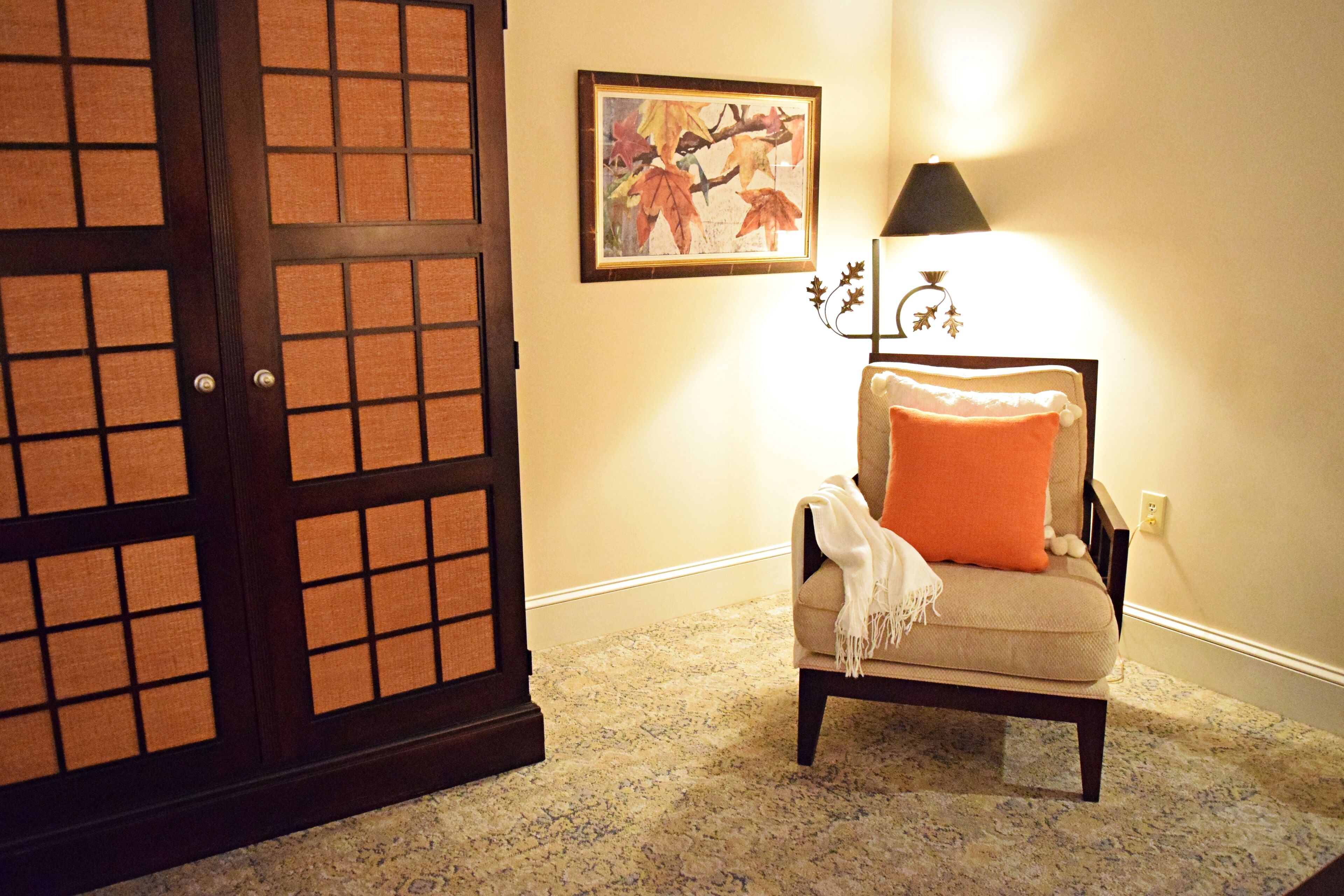 Une pièce dotée d’une porte coulissante de style japonais traditionnel, d’un tableau encadré au mur, d’une lampe et d’une chaise avec un coussin.