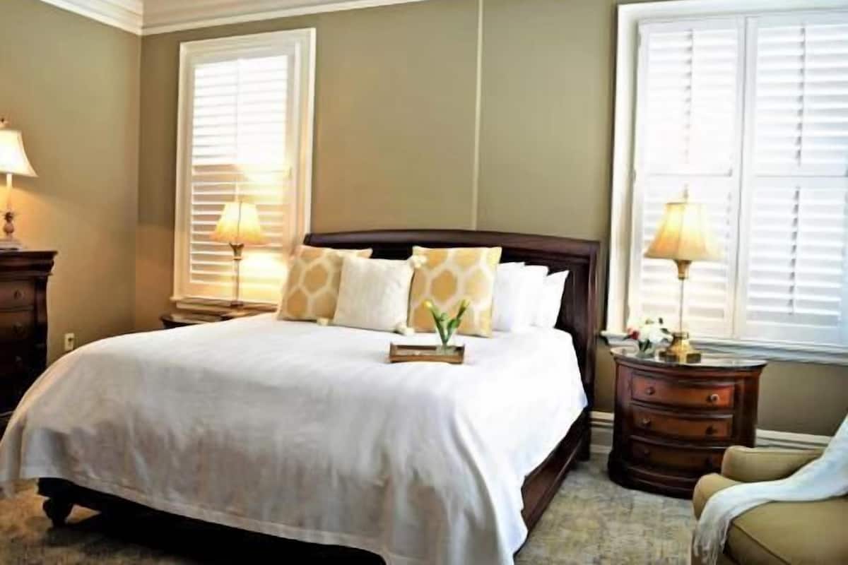 A bedroom with a large bed, two bedside tables with lamps, and a window with blinds.