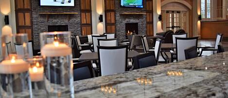 A restaurant with a stone fireplace, multiple TVs, and candle-lit tables.