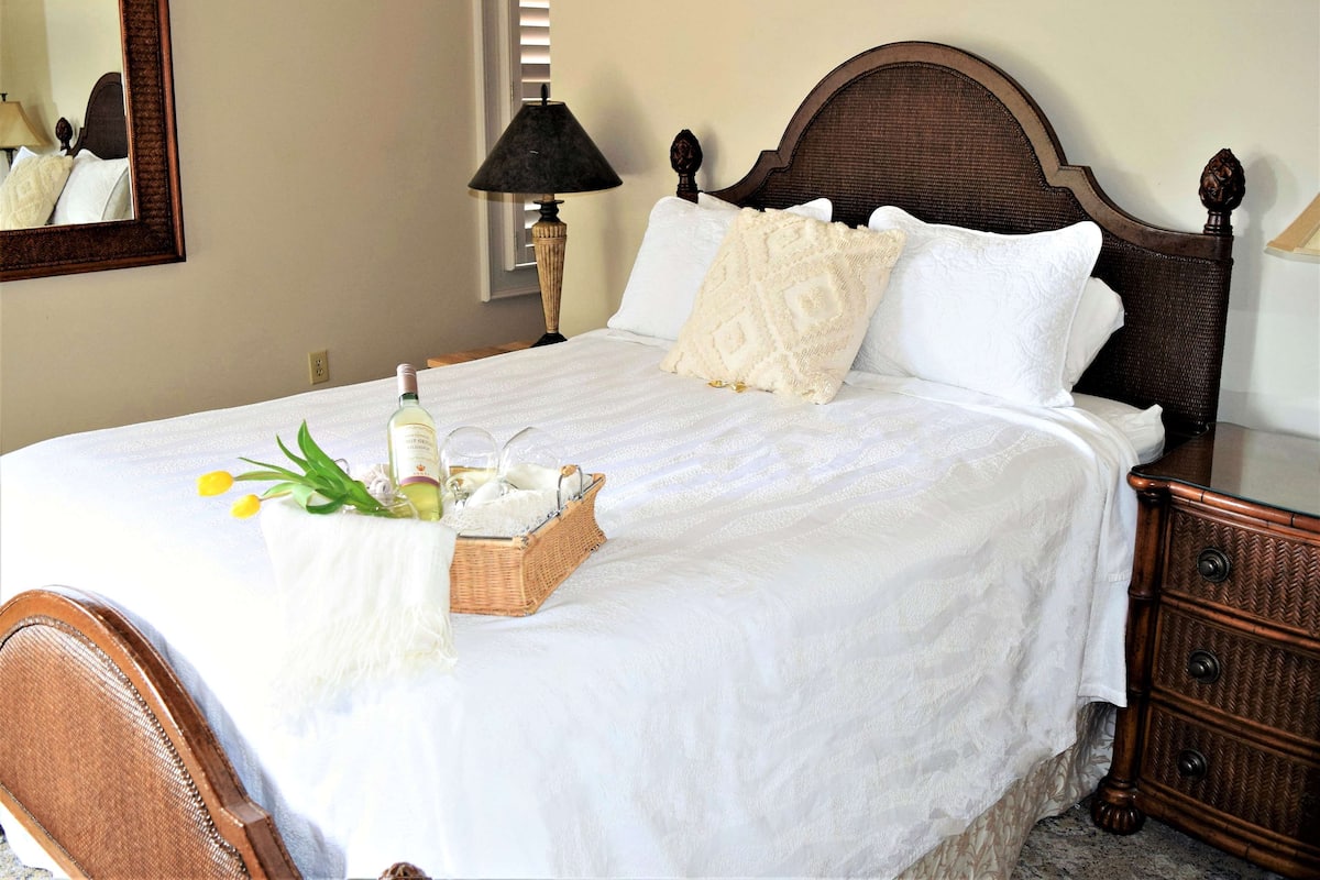 A neatly made bed with a white bedspread, a wooden headboard, and a bedside table with a lamp.