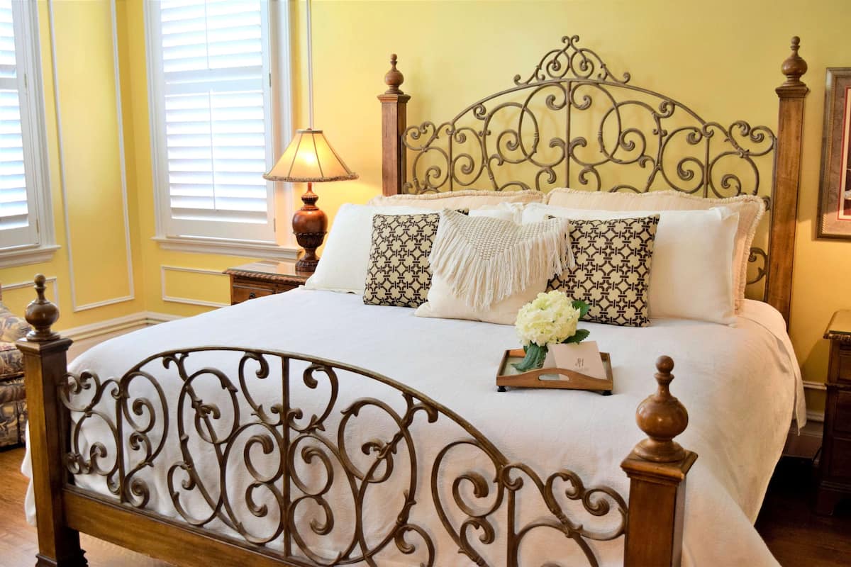 A neatly made bed with a decorative headboard, a bedside lamp, and a tray with flowers.