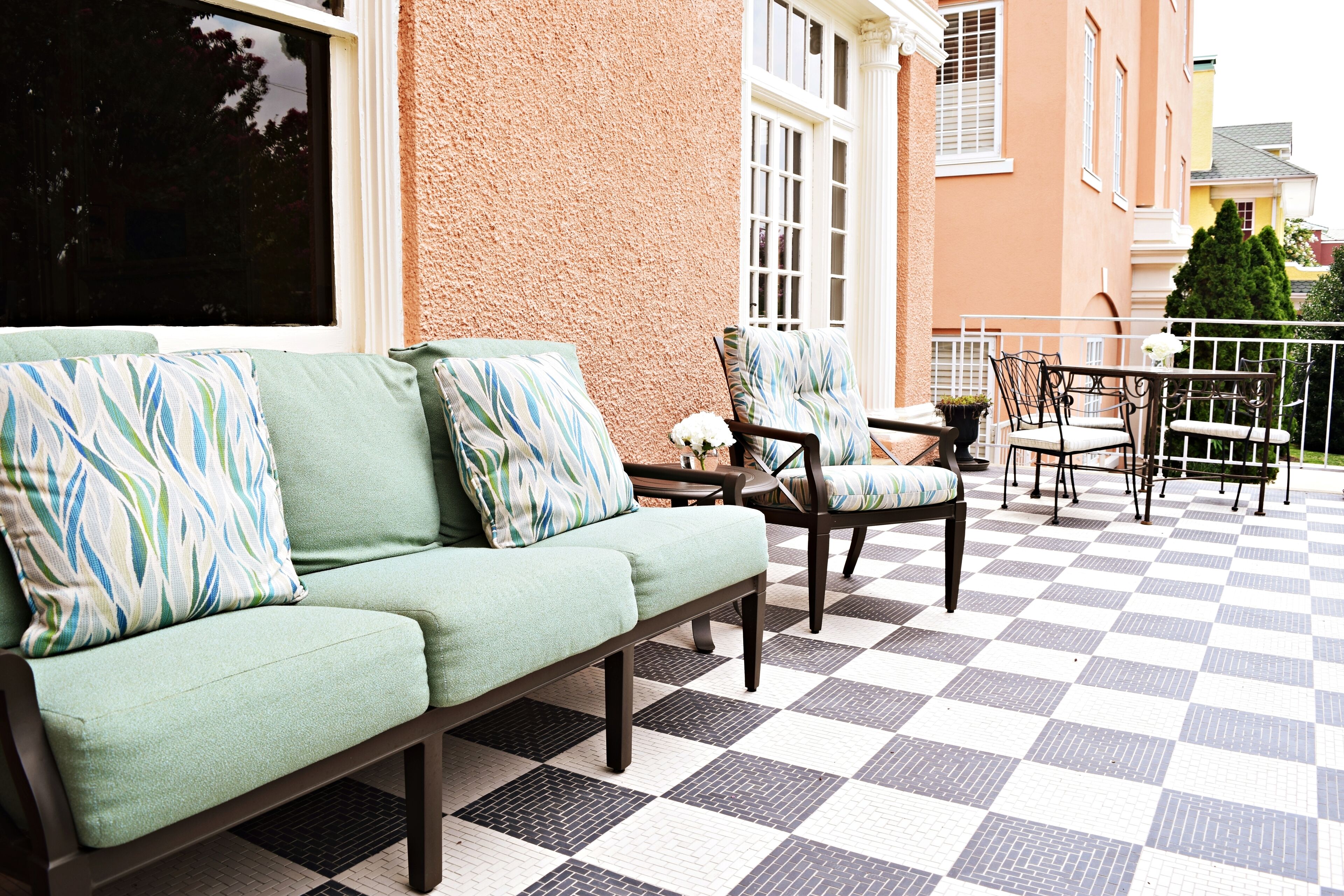 A checkered outdoor patio with a green sofa and chairs, a small table, and a railing.