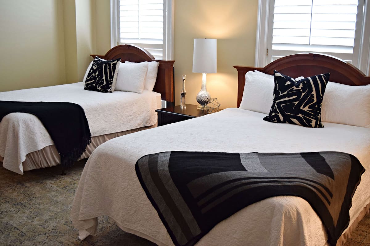 Two single beds with headboards, a bedside lamp, and a window with blinds.