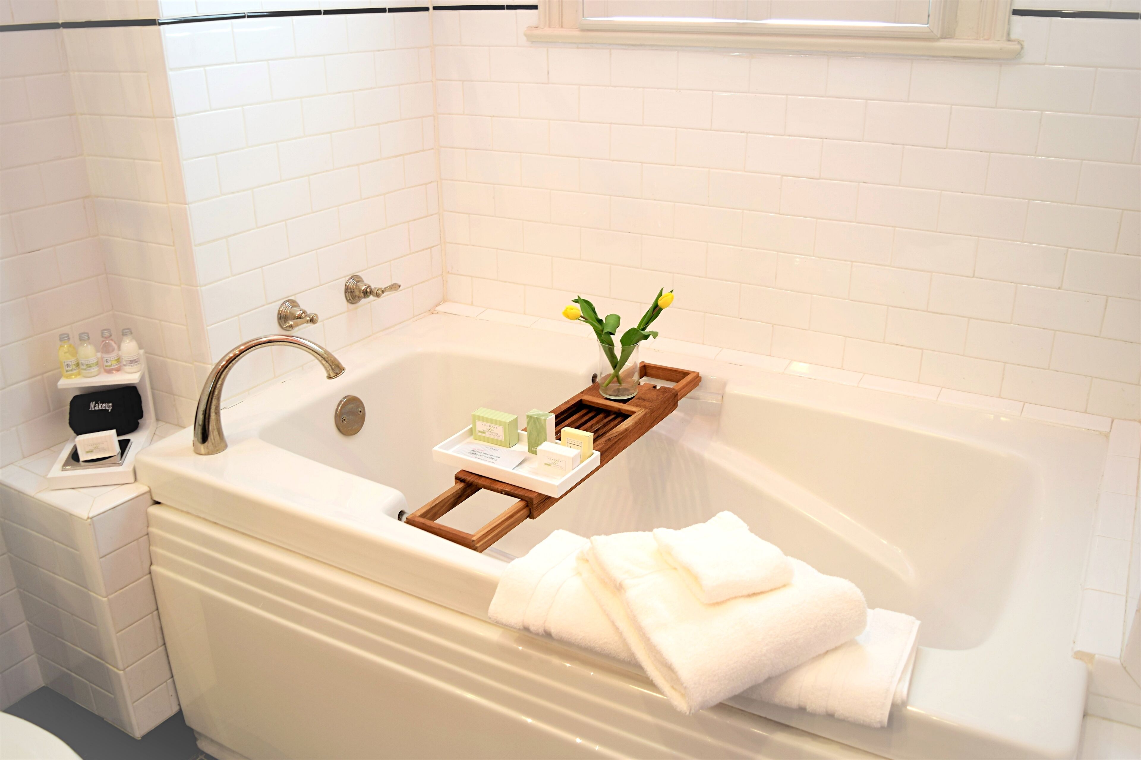 Un baño con una bañera blanca, una bandeja de madera con artículos de aseo y un florero con flores.