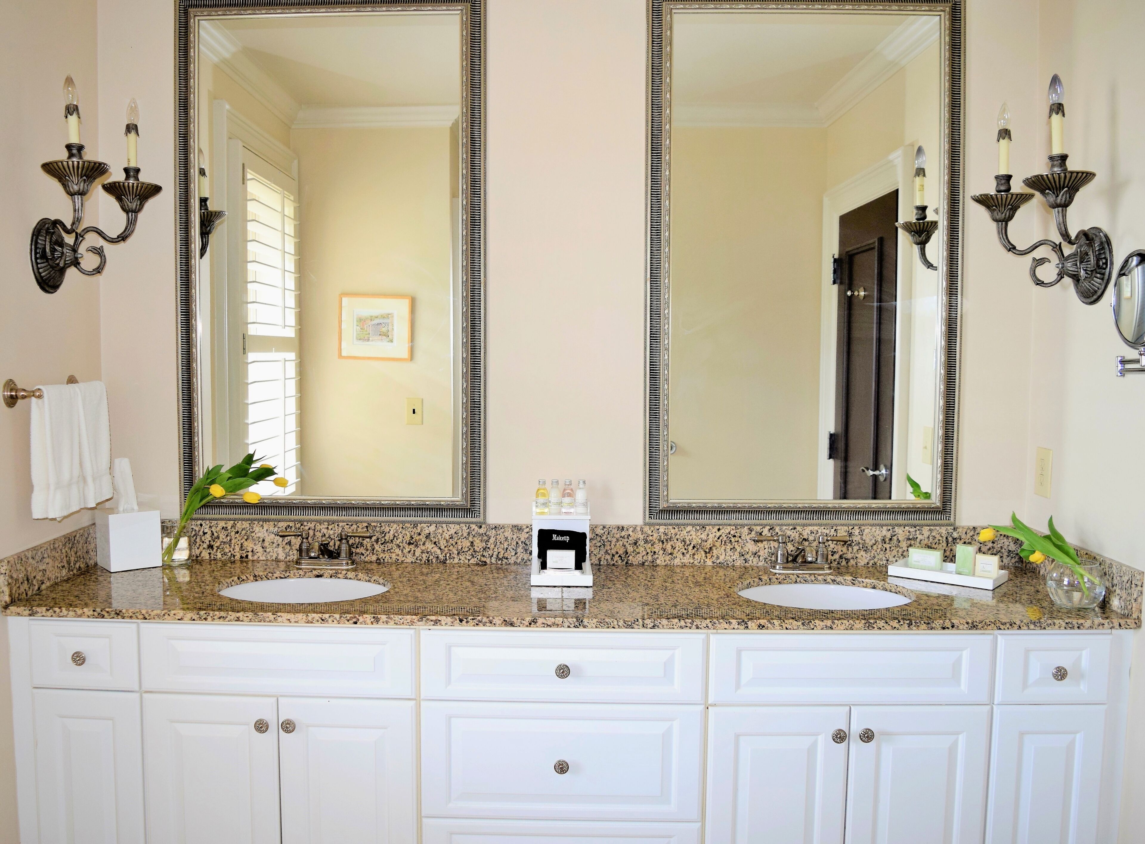 Un bagno con due lavabi, un mobile contenitore con cassetti, uno specchio grande, applique e un quadro appeso alla parete.