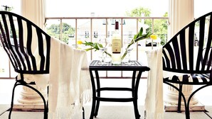A balcony with two black metal chairs, a table with a bottle and glasses, and a view of buildings and greenery. - JH Adams Inn, Trademark Collection by Wyndham (High Point)