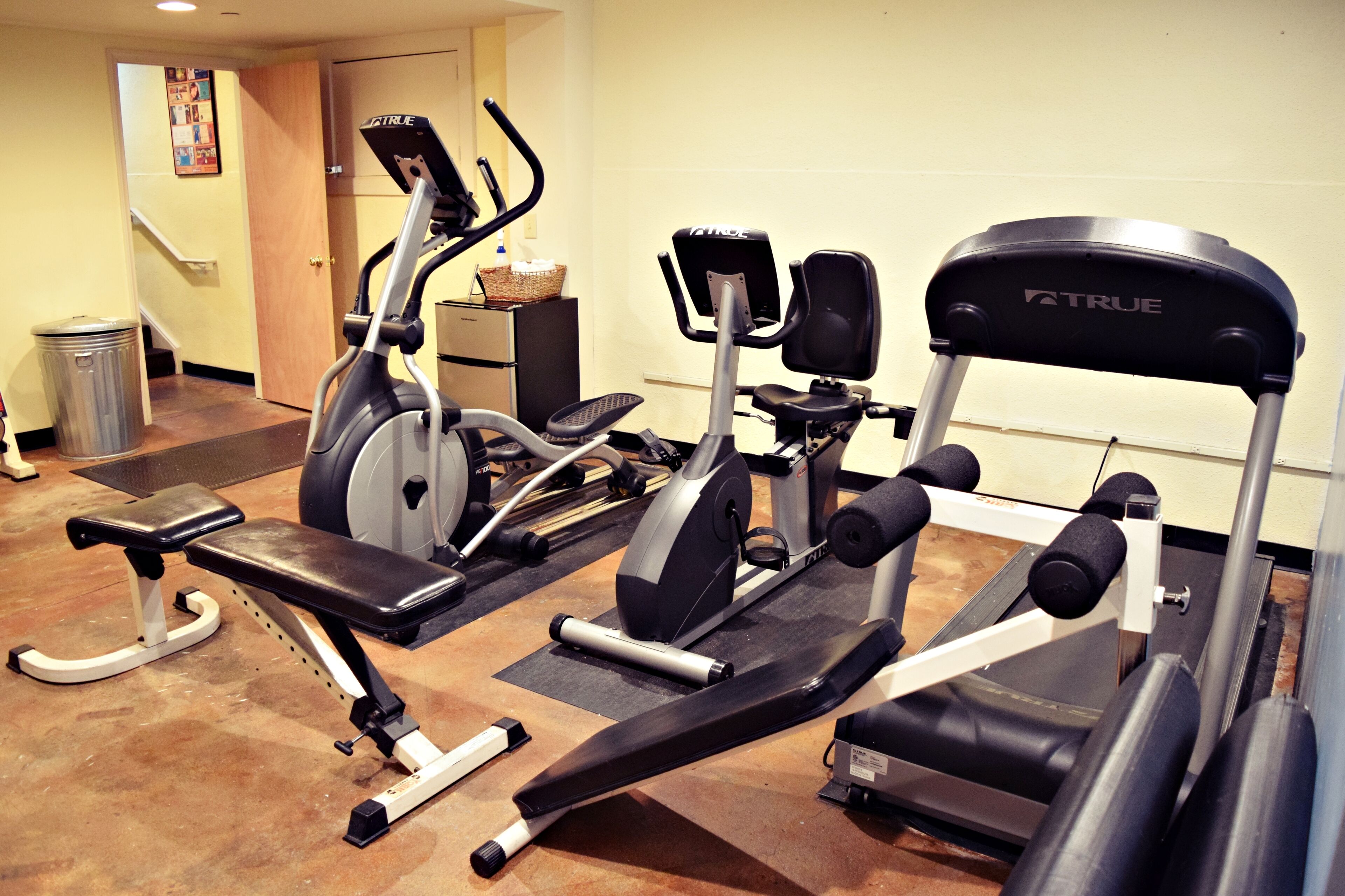 Une salle de sport équipée de divers appareils d’exercice, notamment un tapis de course, un vélo elliptique et des appareils de musculation.