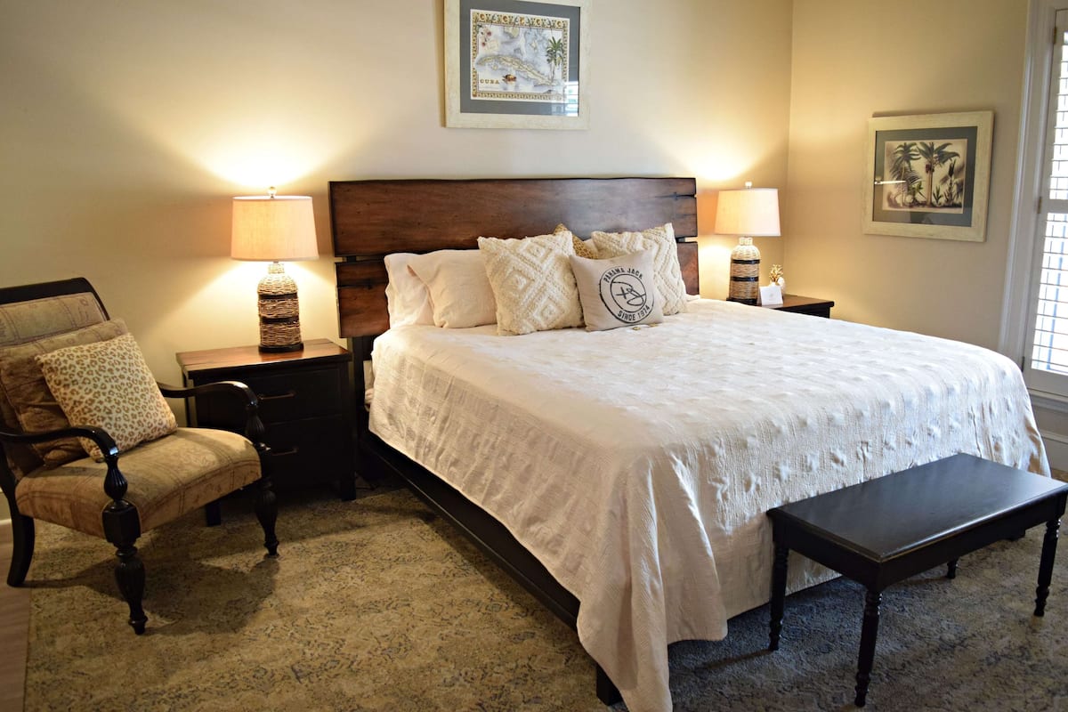A bedroom with a large bed, two bedside tables with lamps, a chair, and a bench.