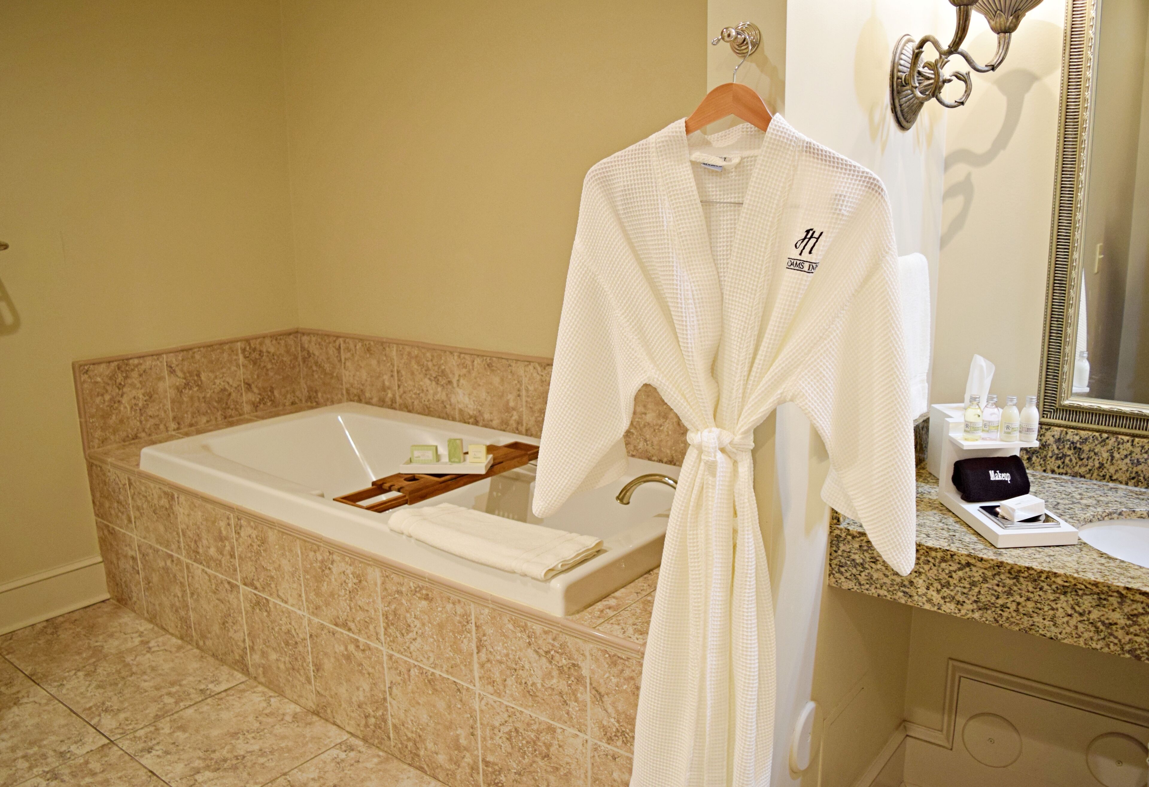 Ein Badezimmer mit einer großen Badewanne, einem Handtuchhalter mit Bademantel und Toilettenartikeln auf der Ablagefläche.