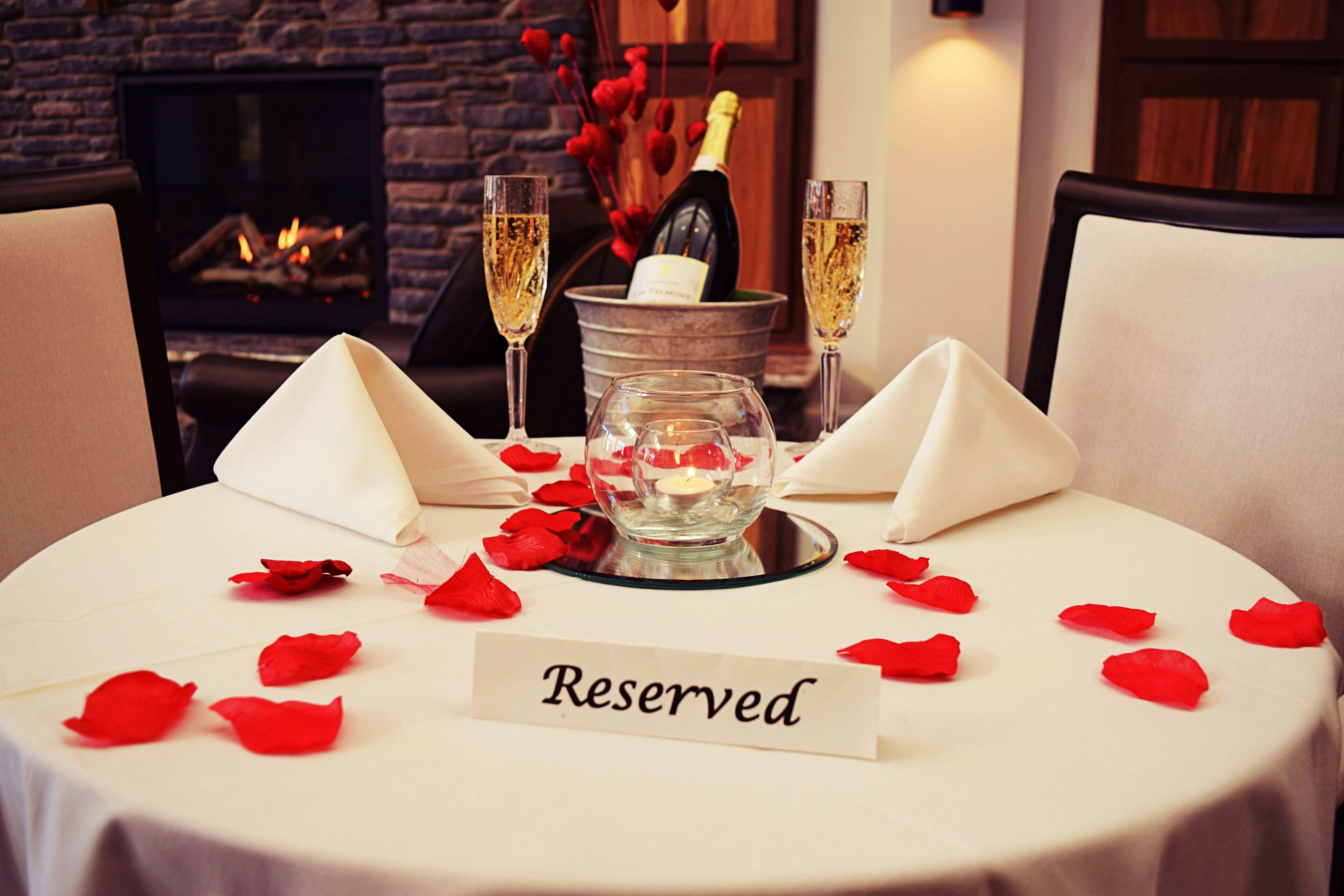 A table set for two with a "Reserved" sign, champagne glasses, a candle, and rose petals.