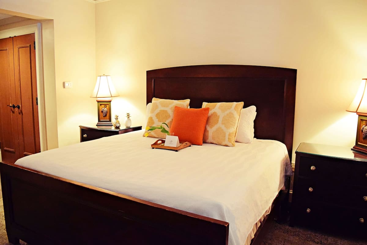 A neatly made bed with a wooden headboard, two bedside tables with lamps, and a door in the background.
