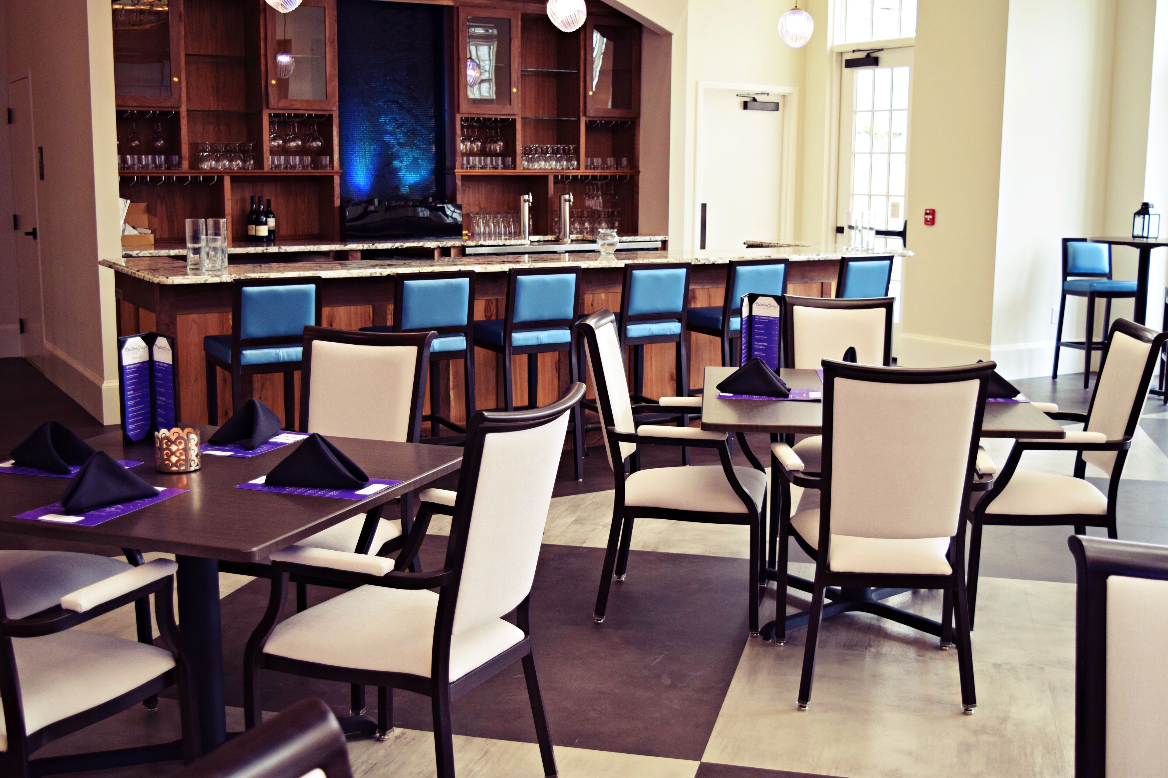 A restaurant with a bar area, multiple tables and chairs, and a checkered floor.