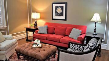 A living room with a red sofa, a brown ottoman, a patterned armchair, and a small table with a lamp.