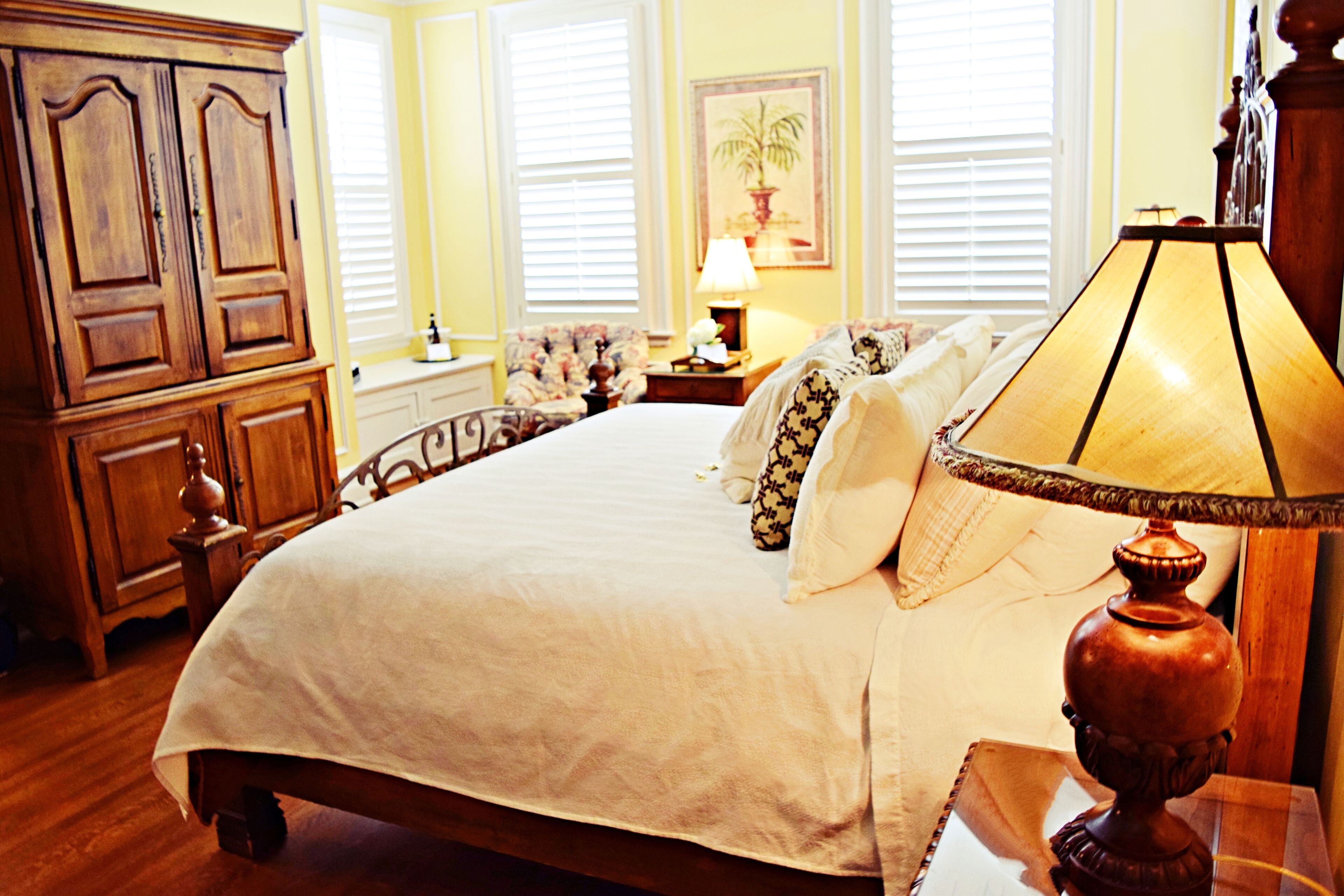 A large bed with a wooden headboard, a nightstand with a lamp, and a floral chair.