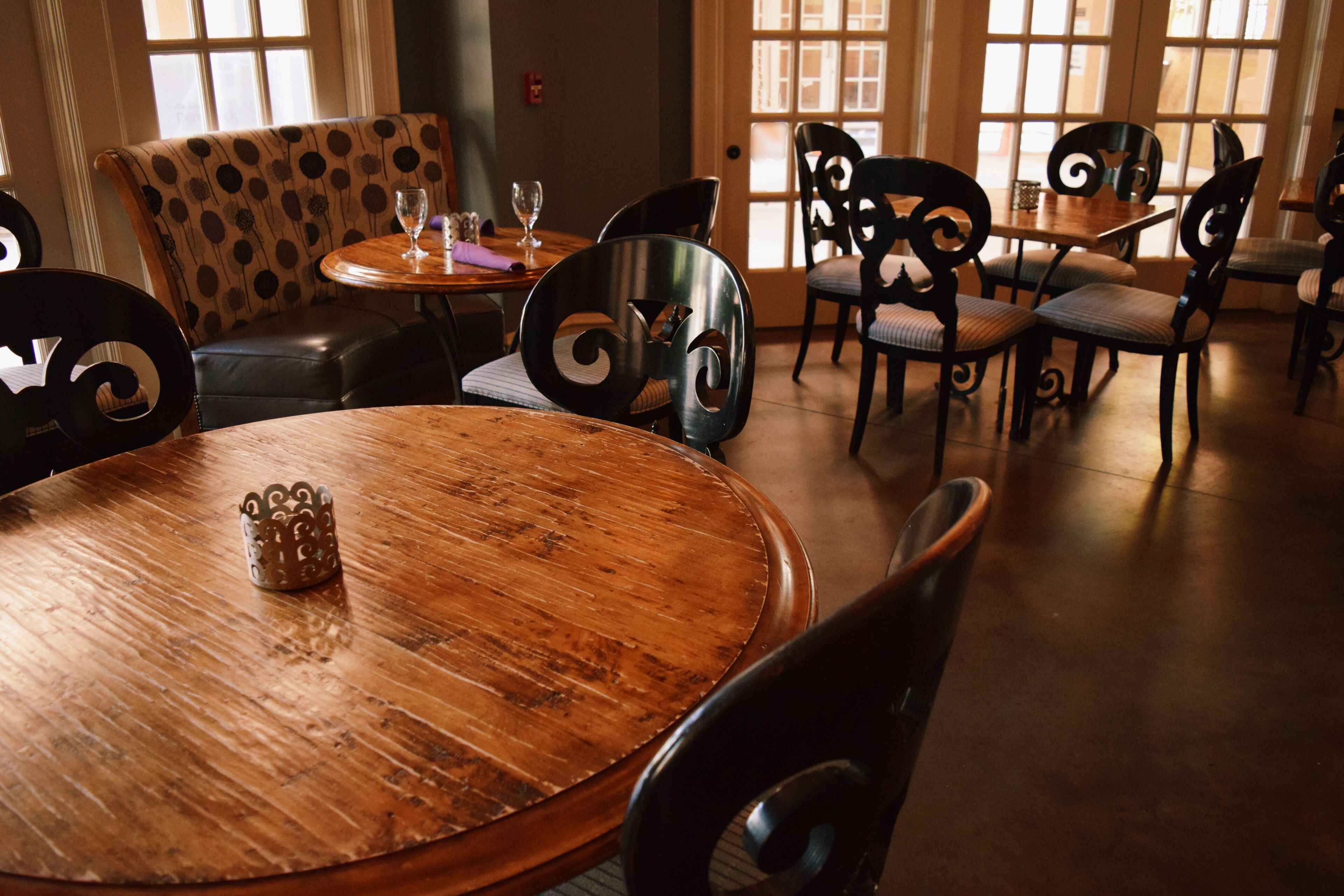 Un comedor con mesas redondas de madera, sillas negras con diseños elaborados y un sofá estampado.