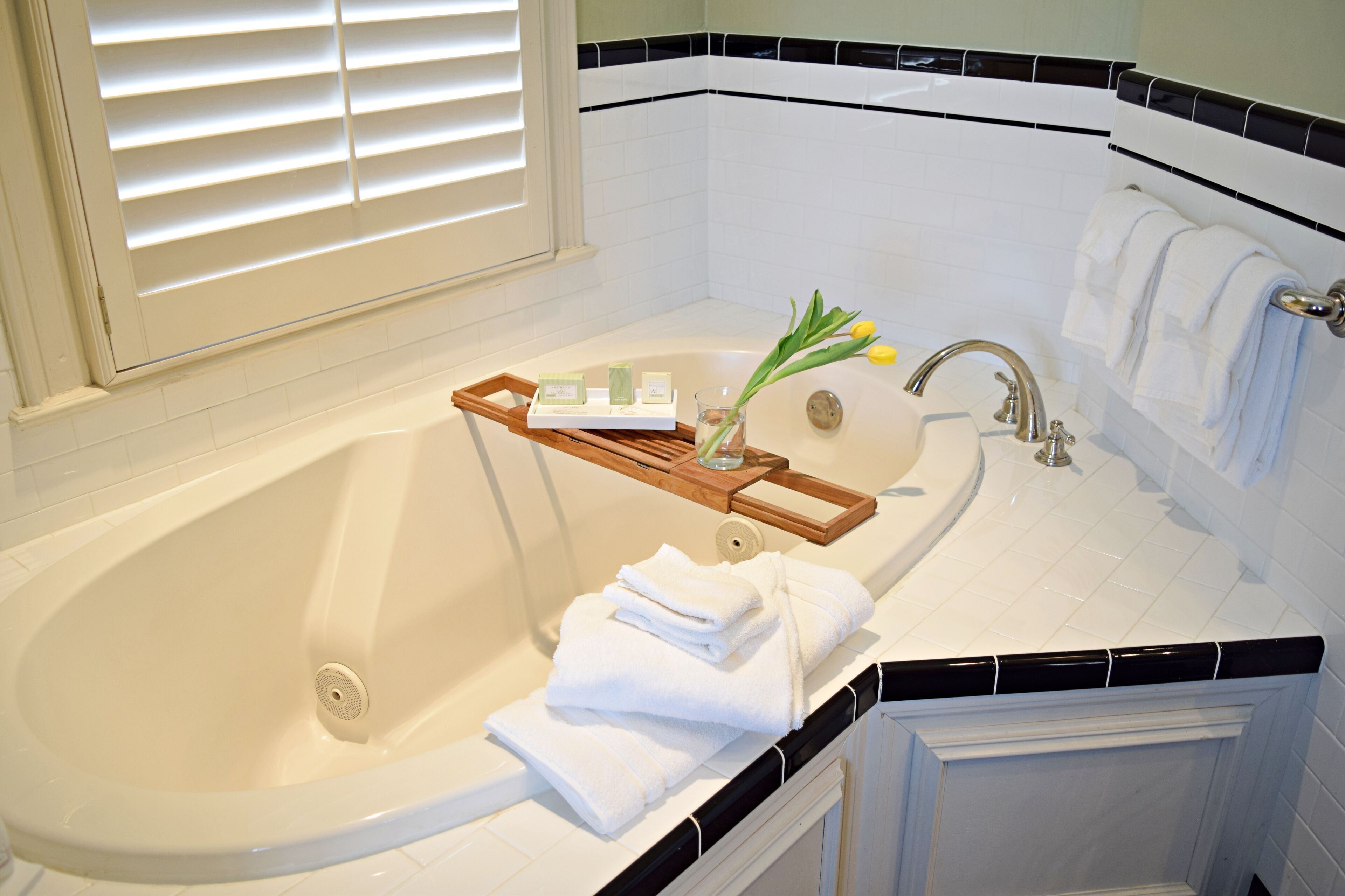 A bathroom with a bathtub, a wooden tray with toiletries, and towels.