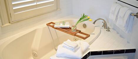A bathroom with a bathtub, a wooden tray with toiletries, and towels.