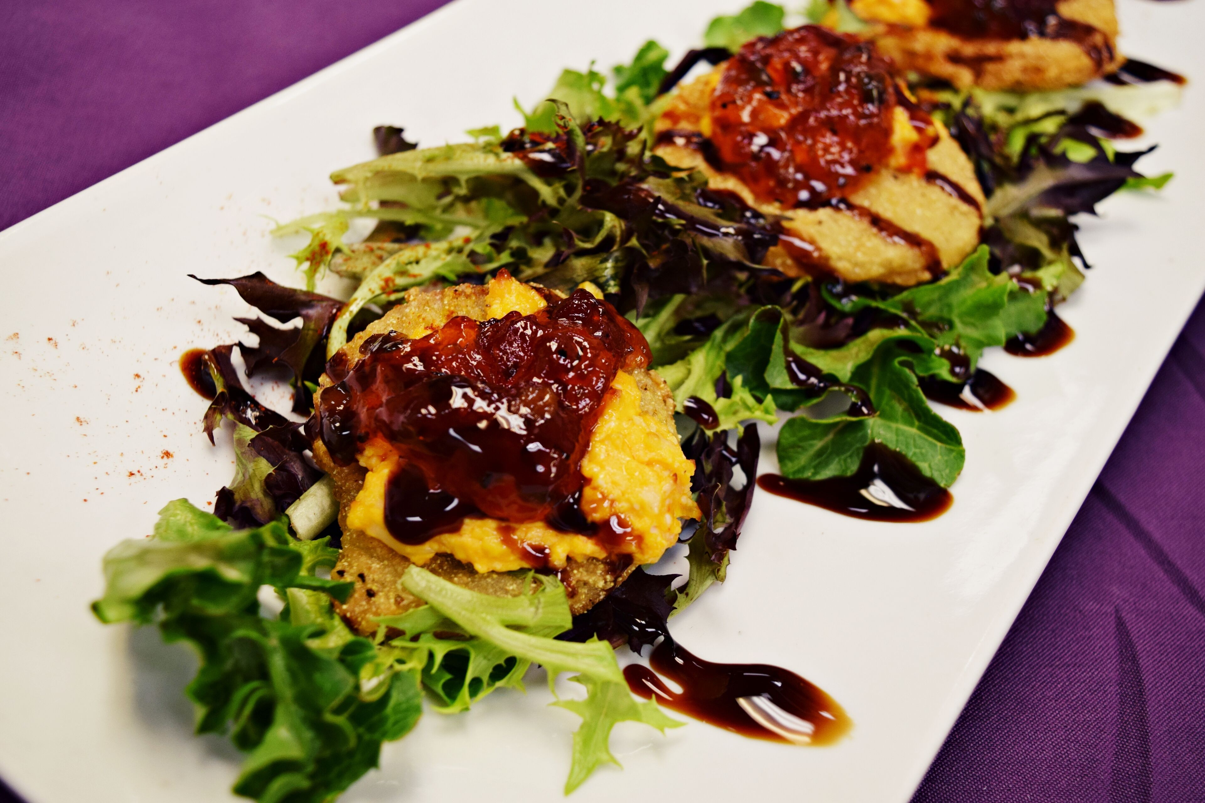 A white plate with a salad and two pieces of bread topped with a dark sauce.
